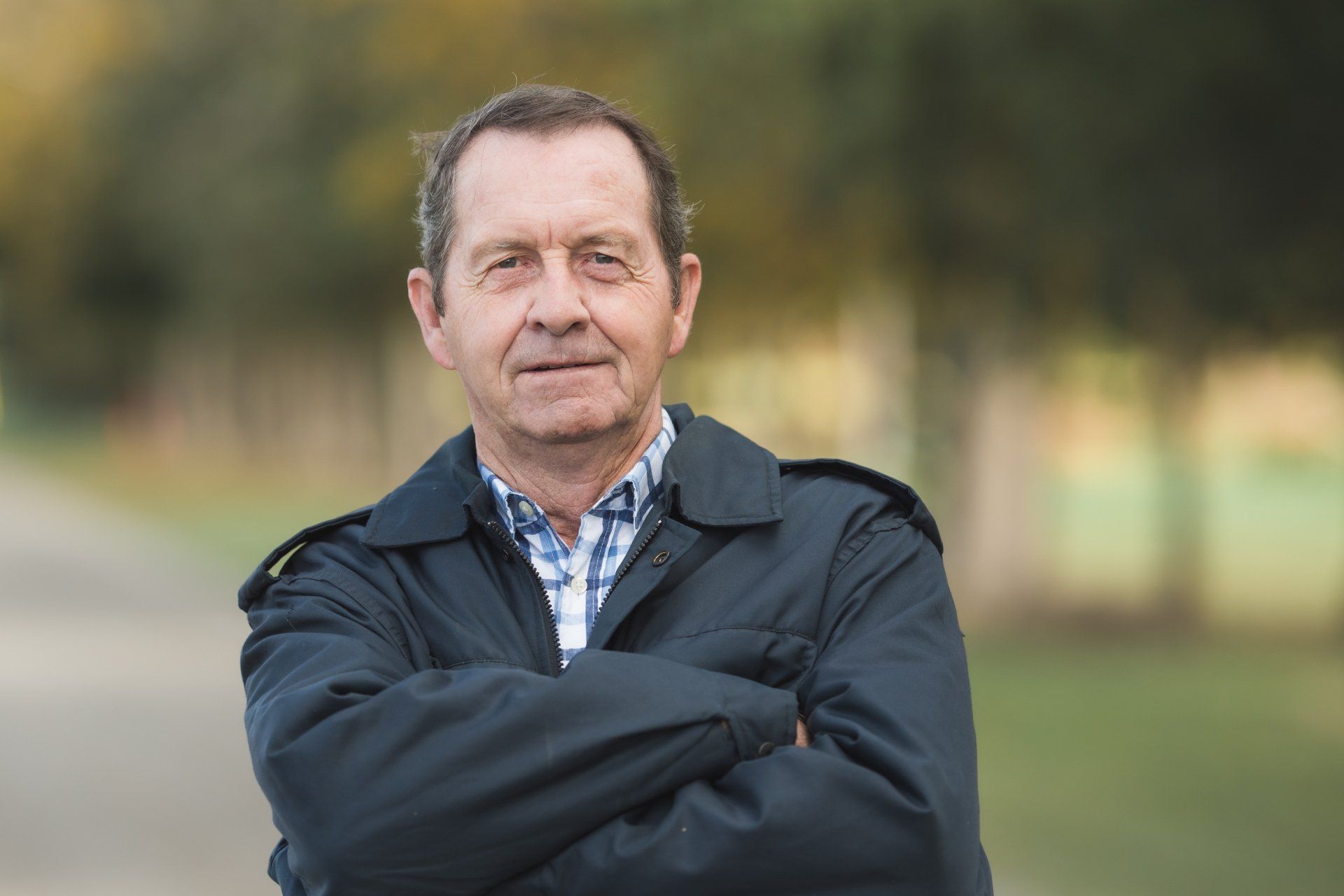 A man in a blue jacket is standing with his arms crossed.