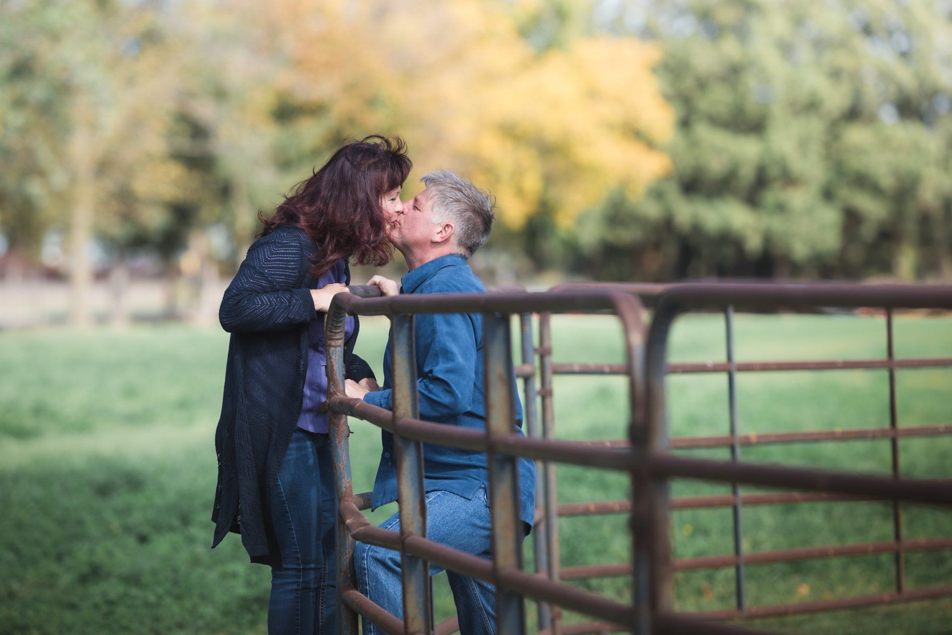 A man and a woman are kissing on a fence in a field.