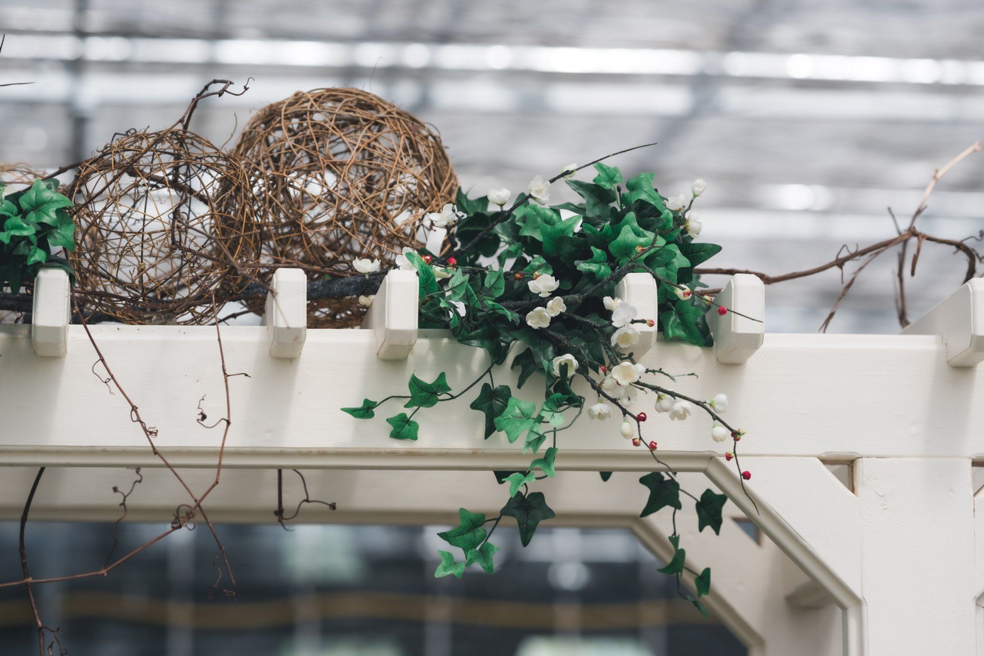 A white pergola with ivy and balls on top of it.