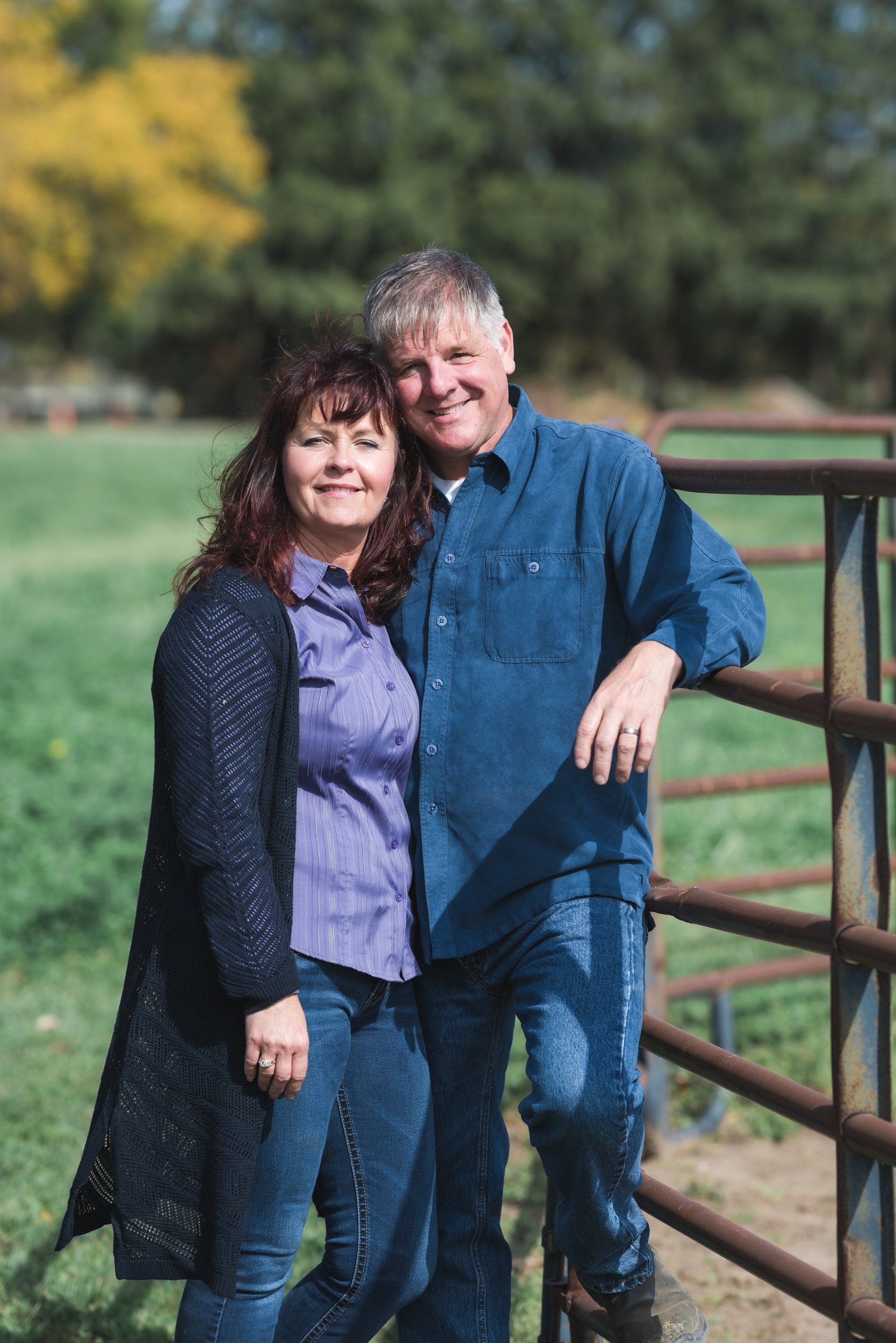 A man and a woman are standing next to a fence in a field.