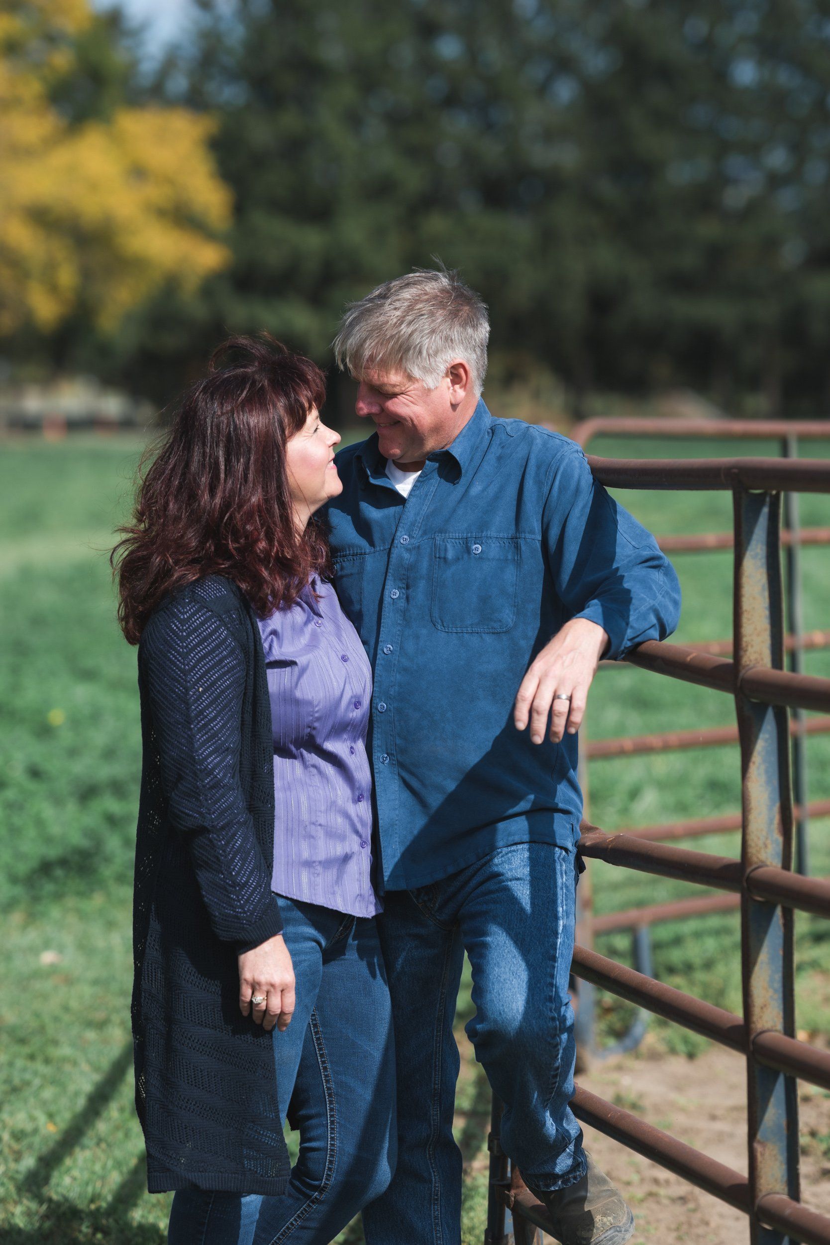 A man and a woman are standing next to a fence in a field.