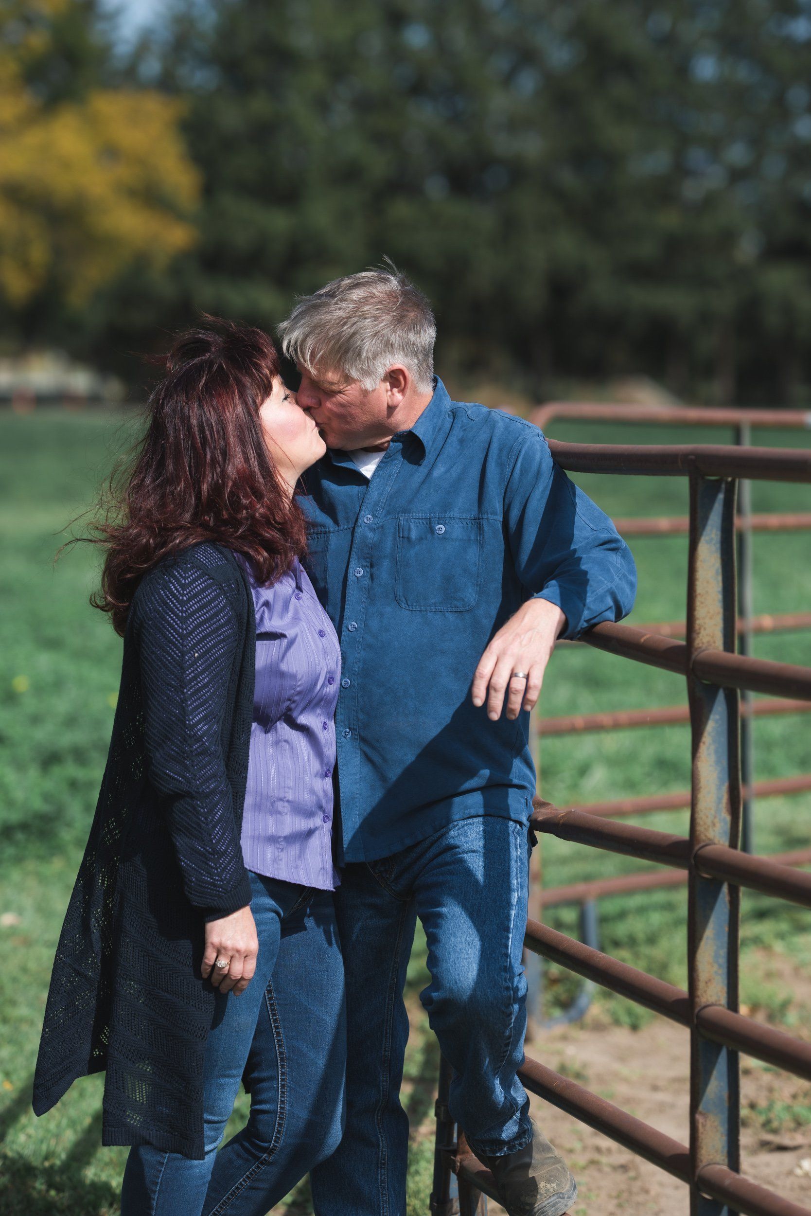 A man and a woman are kissing in front of a fence.