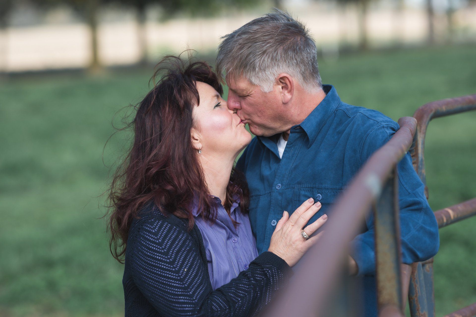 A man and a woman are kissing in front of a fence.