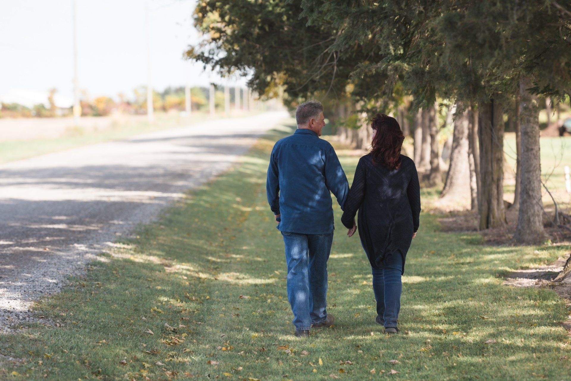A man and a woman are walking down a dirt road holding hands.