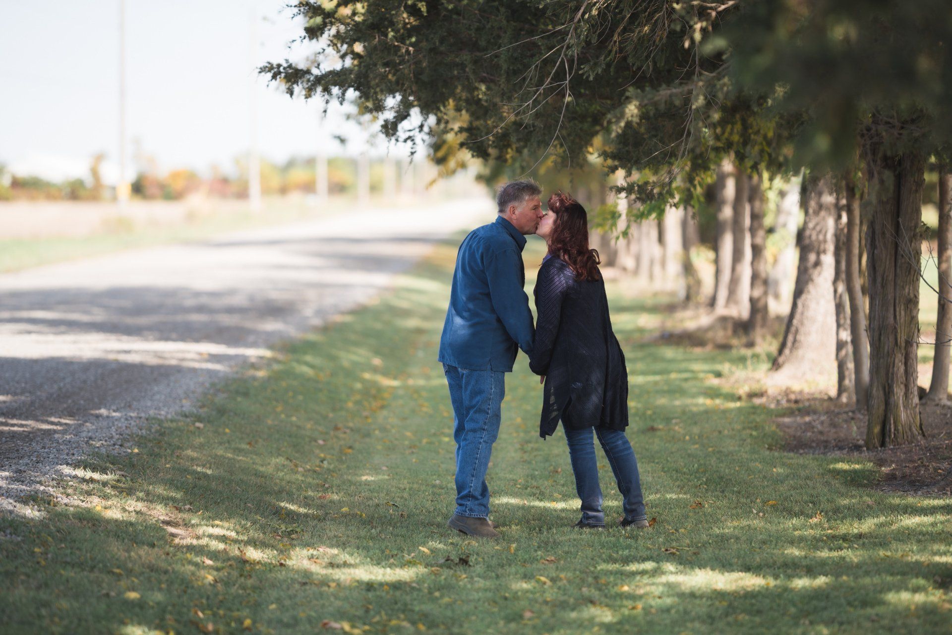 A man and a woman are kissing under a tree on the side of a road.