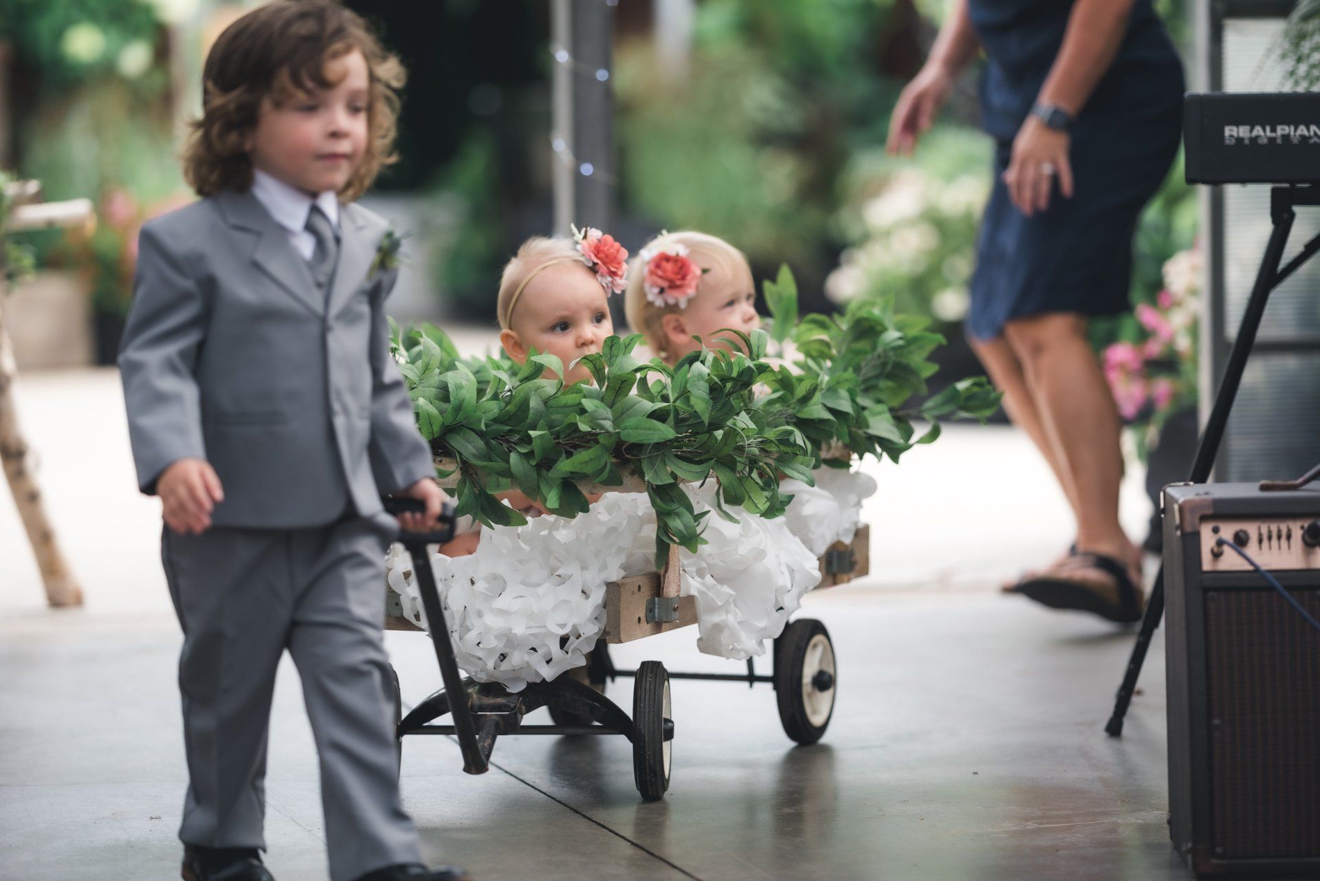 A ring bearer is pushing two flower girls in a wagon.