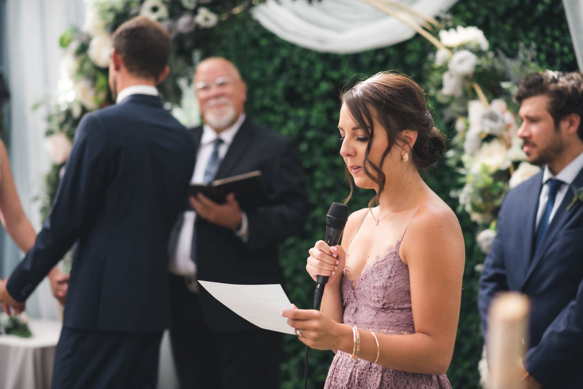 A woman is giving a speech at a wedding ceremony while holding a microphone.