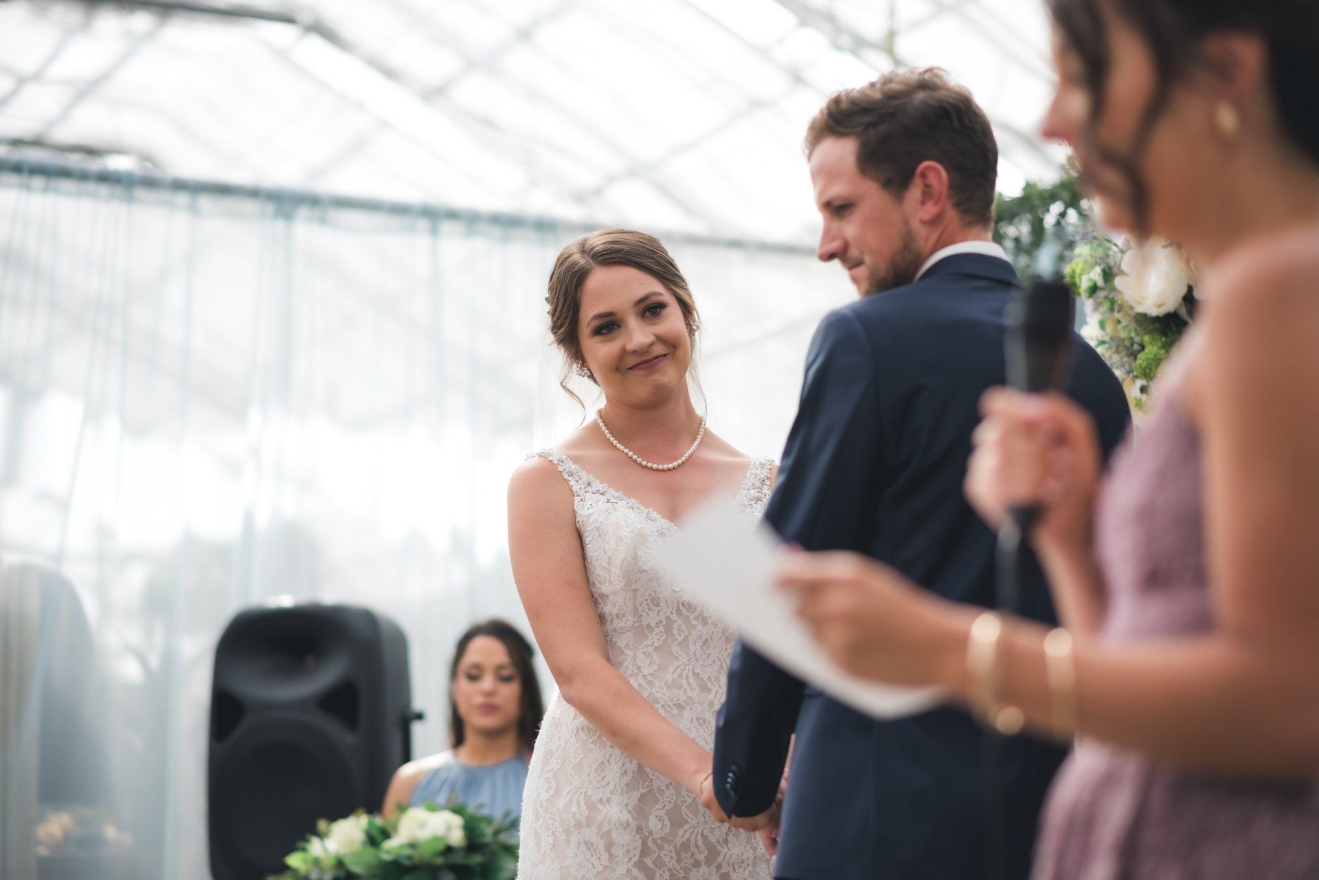 A bride and groom are holding hands during their wedding ceremony in a greenhouse.