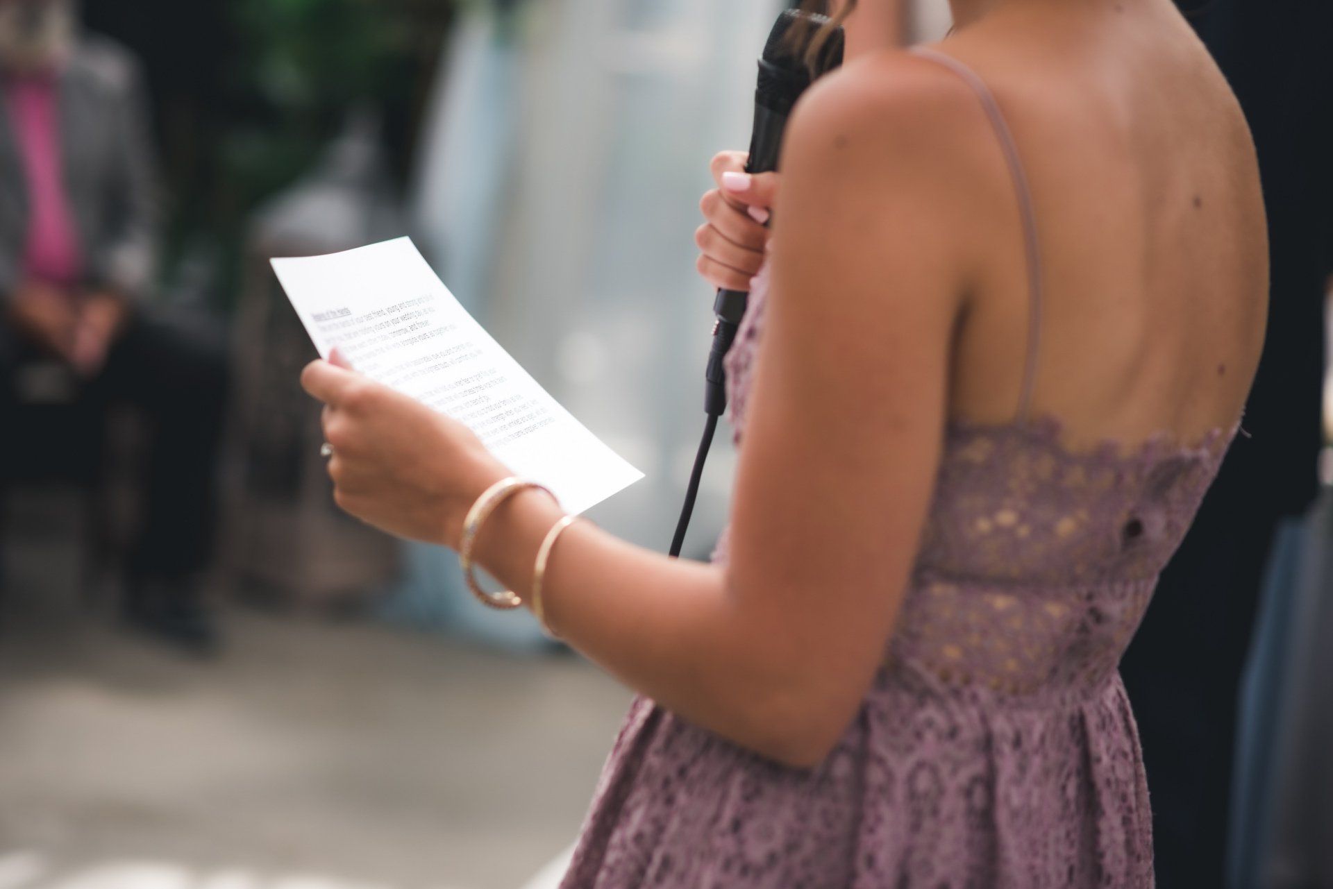 A woman in a purple dress is holding a microphone and reading a piece of paper.