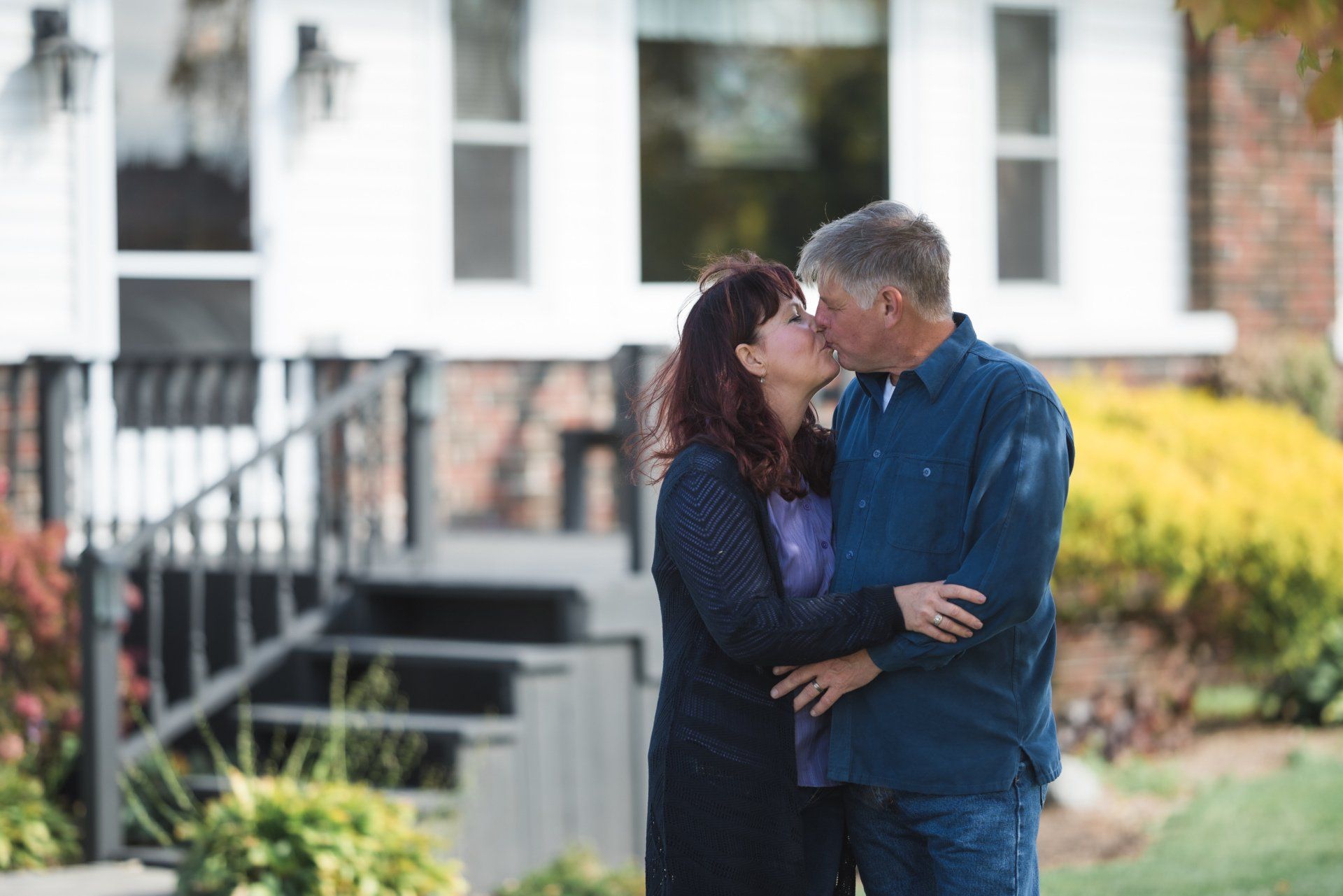 A man and woman are kissing in front of a house.