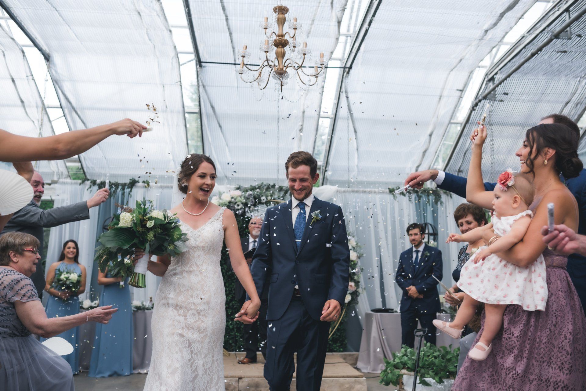 A bride and groom are walking down the aisle while their wedding party throws confetti.