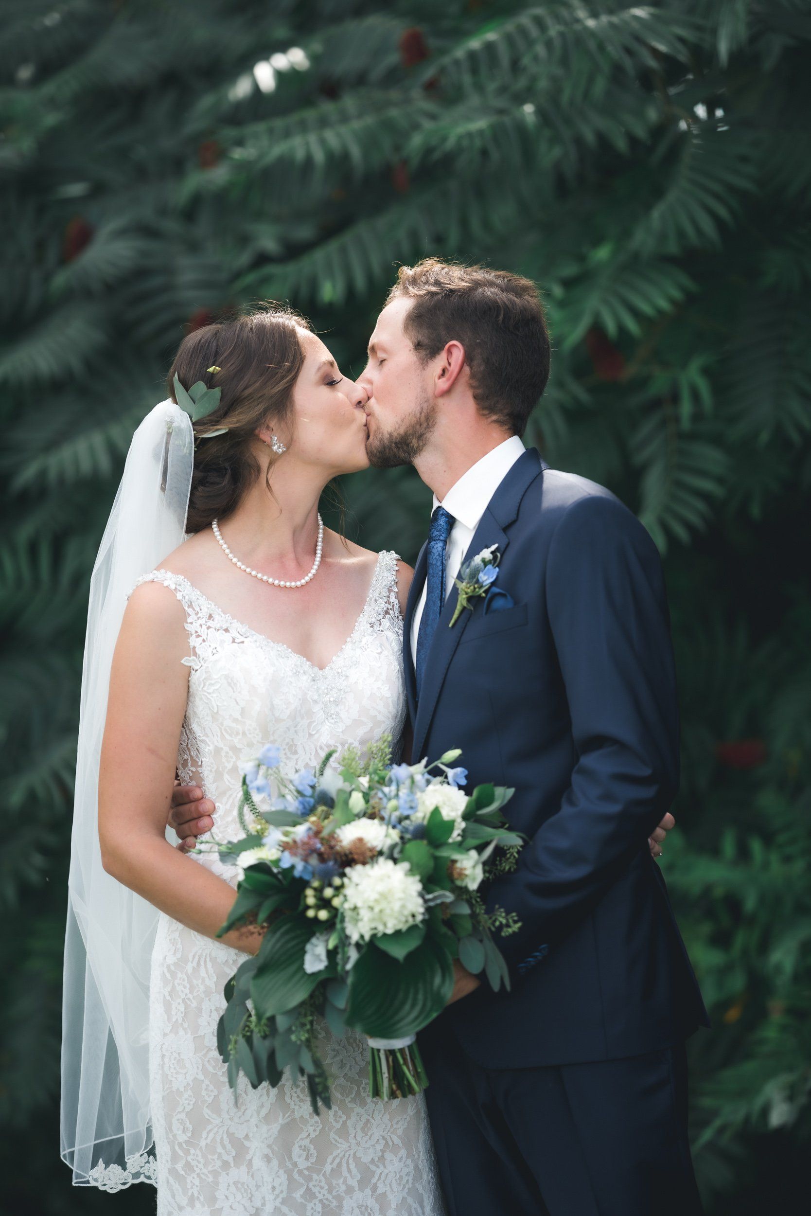 A bride and groom are kissing in front of a tree.