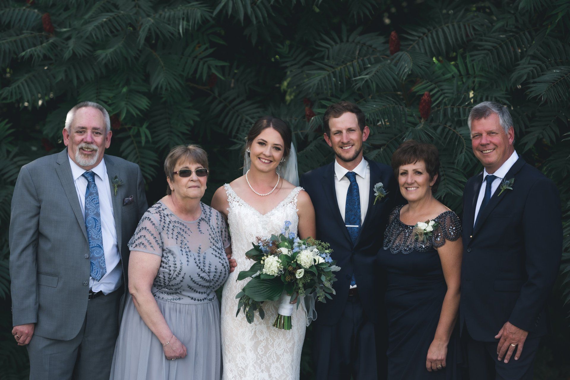 A bride and groom are posing for a picture with their parents.