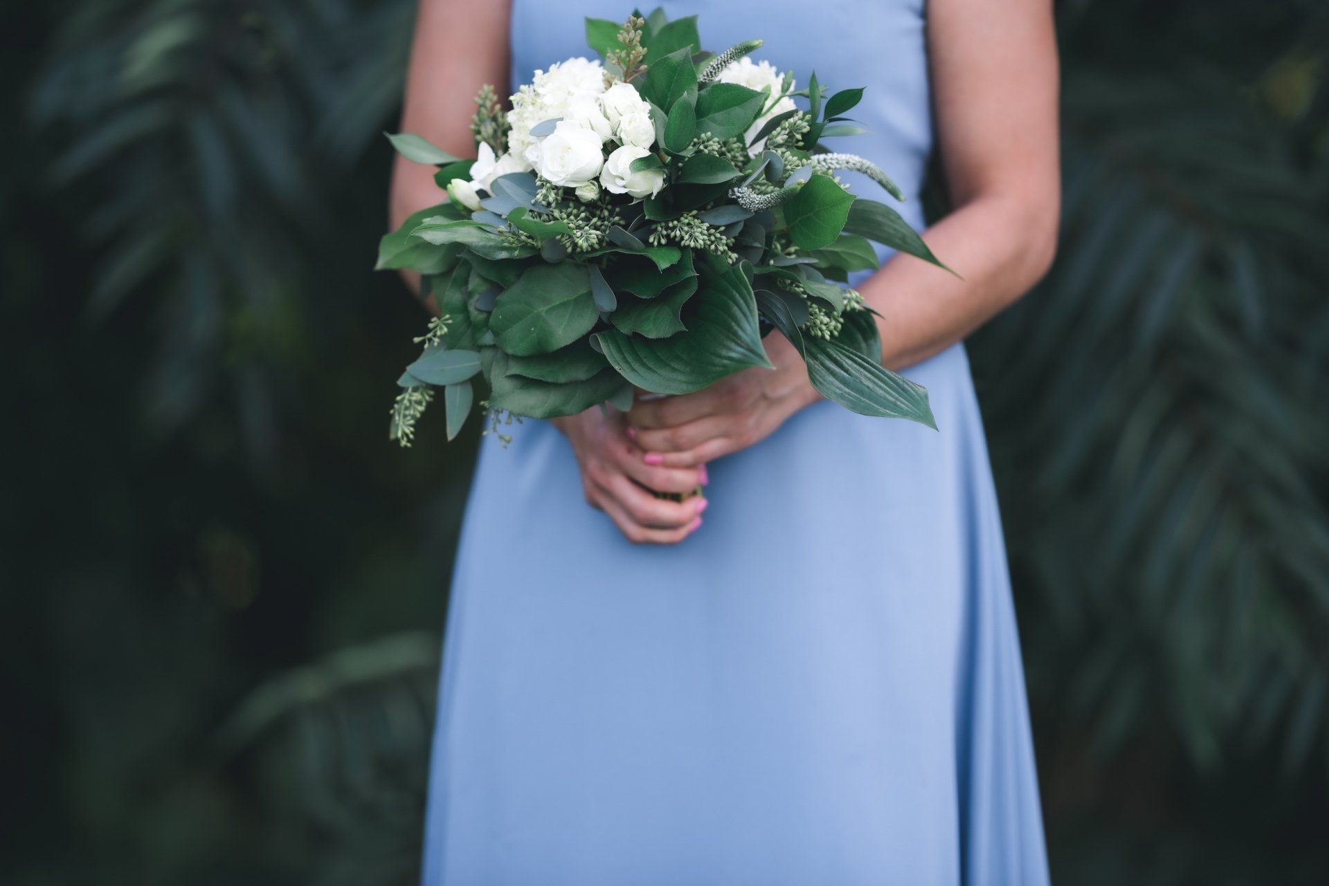A woman in a blue dress is holding a bouquet of white flowers.