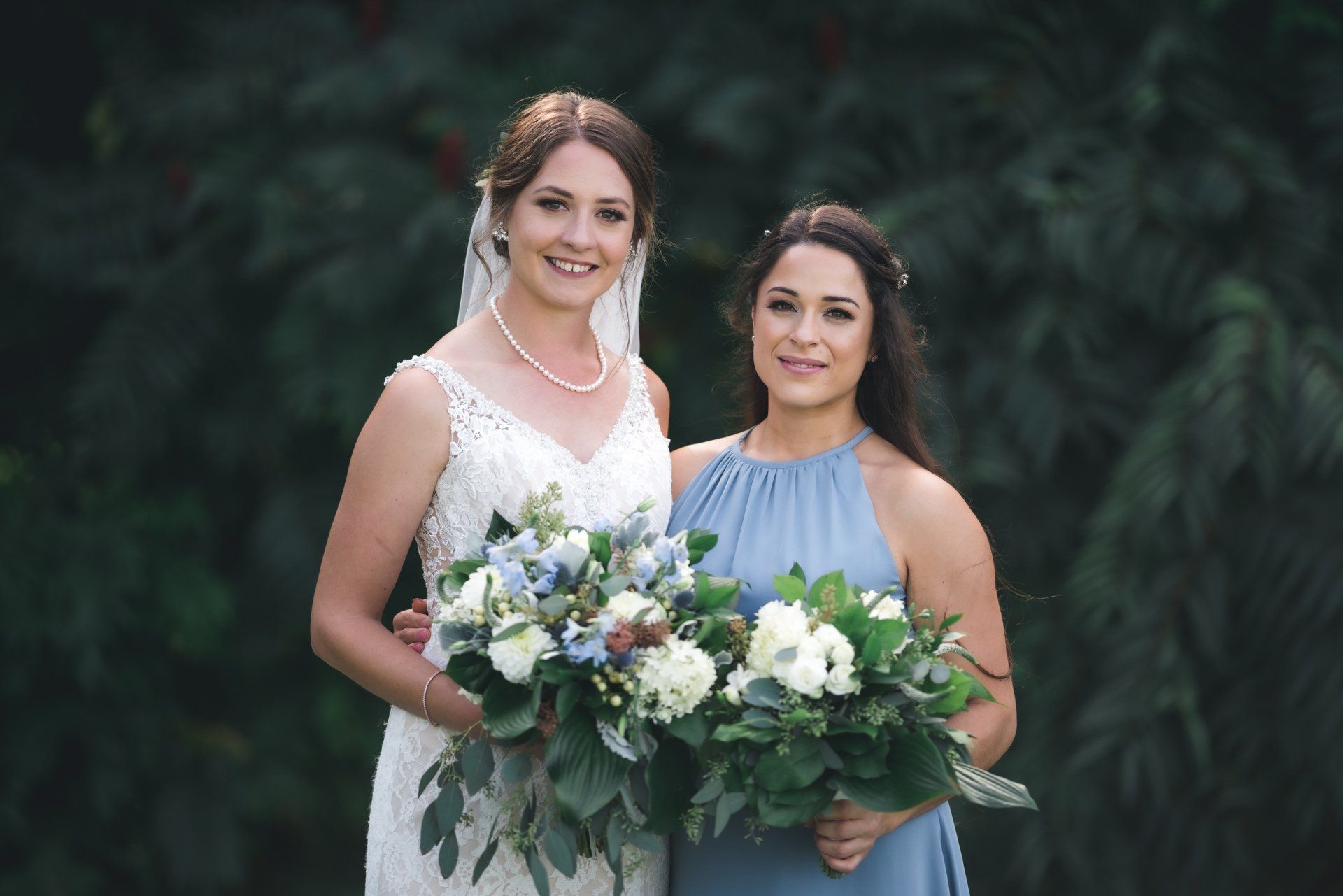 A bride and her bridesmaid are posing for a picture while holding bouquets of flowers.