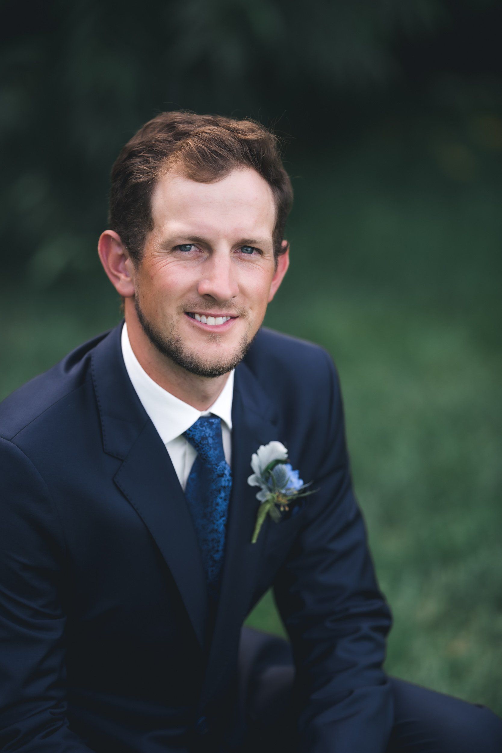 A man in a suit and tie is sitting in the grass.
