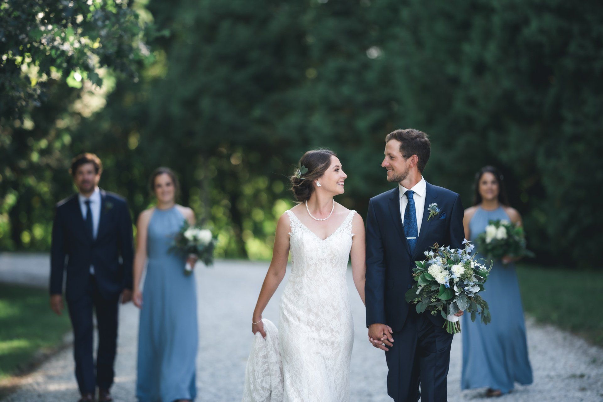 A bride and groom are walking down a dirt road with their wedding party.