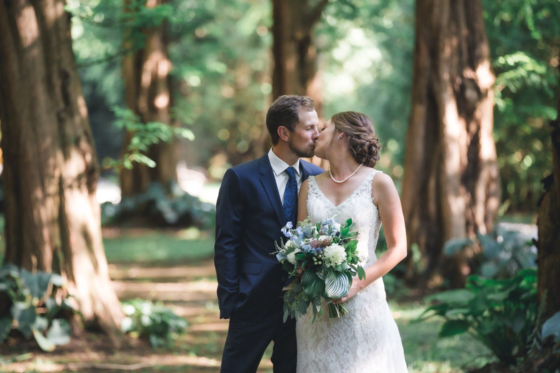 A bride and groom are kissing in the woods.