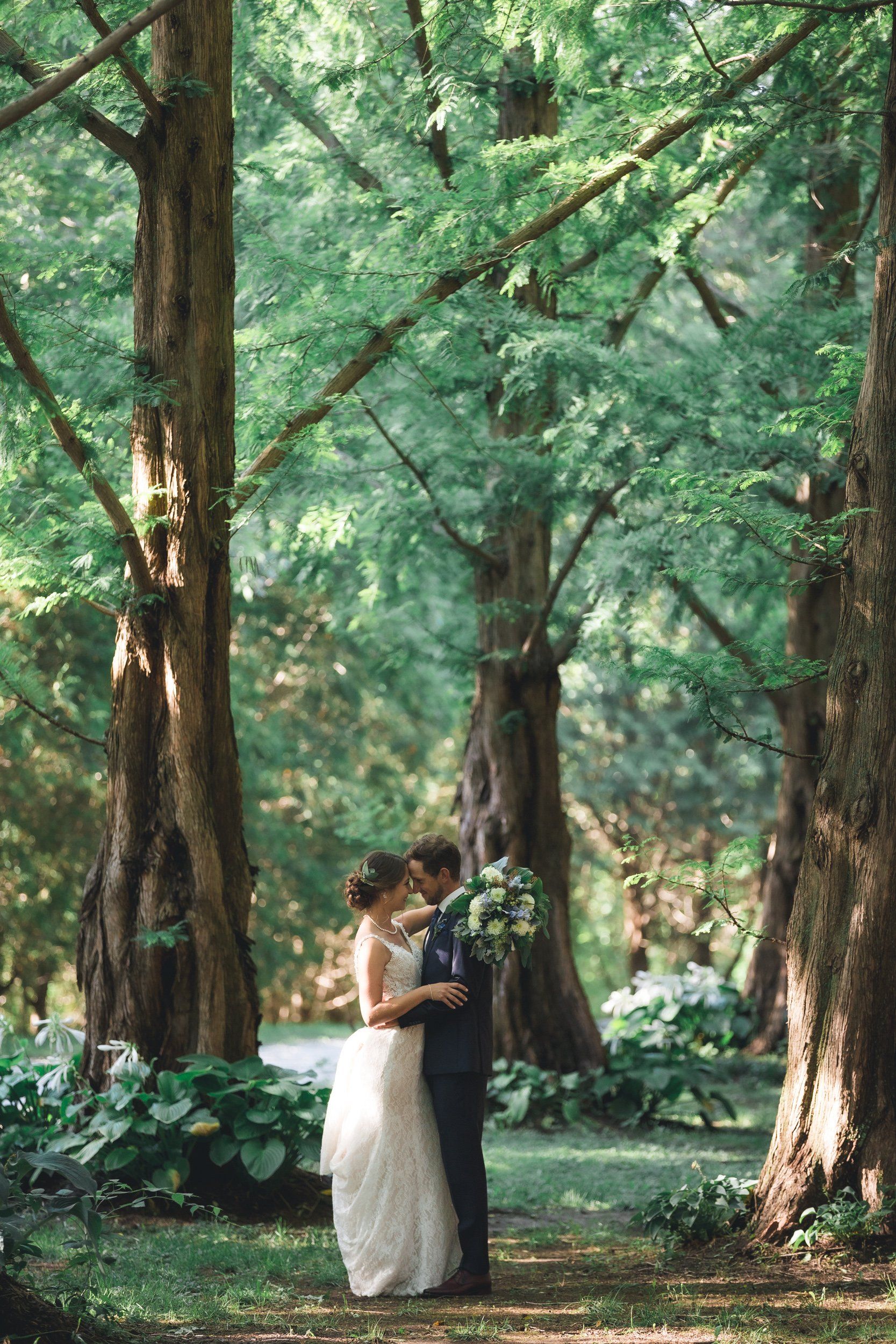 A bride and groom are kissing in the middle of a forest.