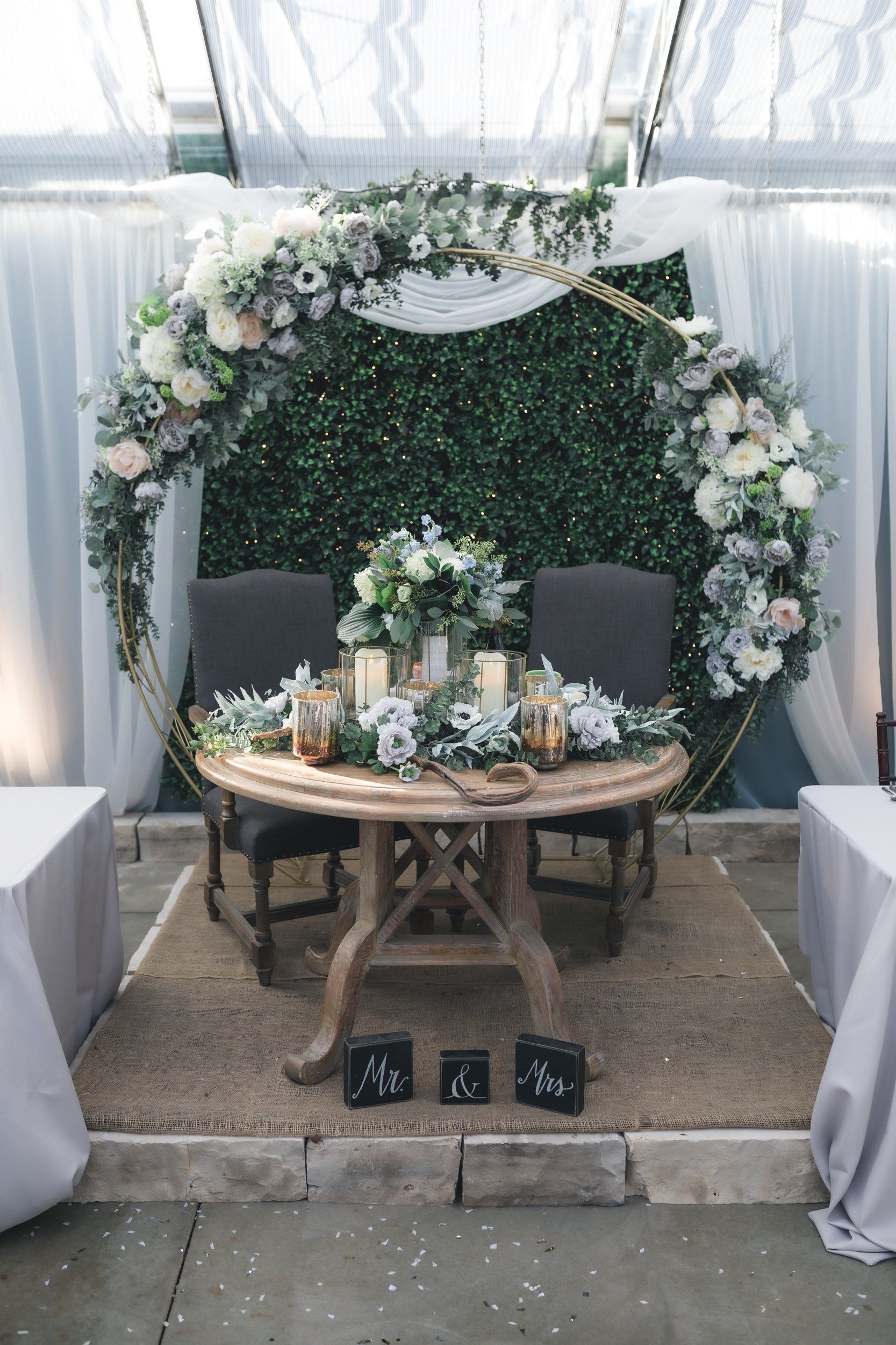 A table and chairs are sitting in front of a floral arch.