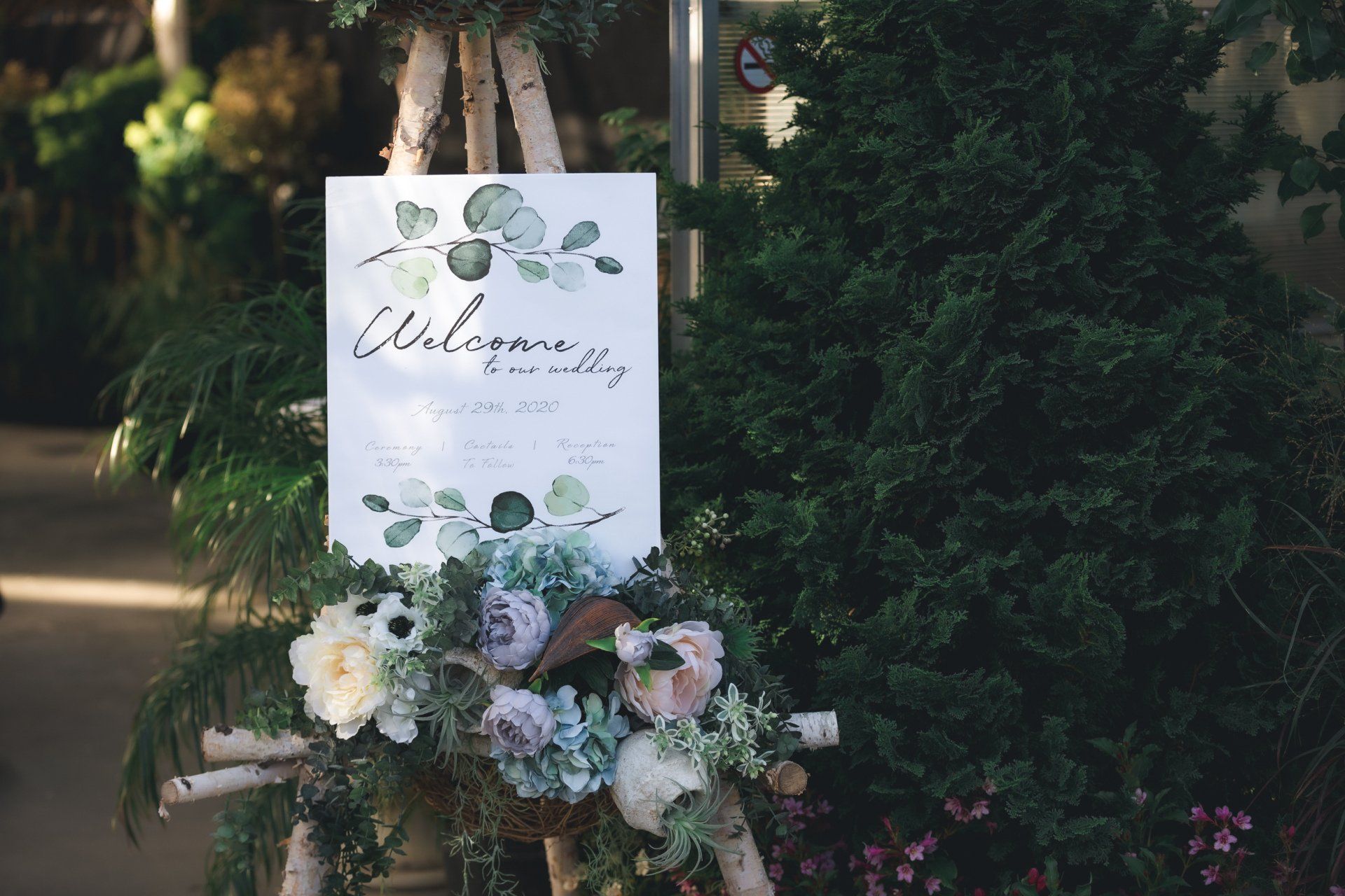 A welcome sign is sitting on a wooden easel surrounded by flowers.