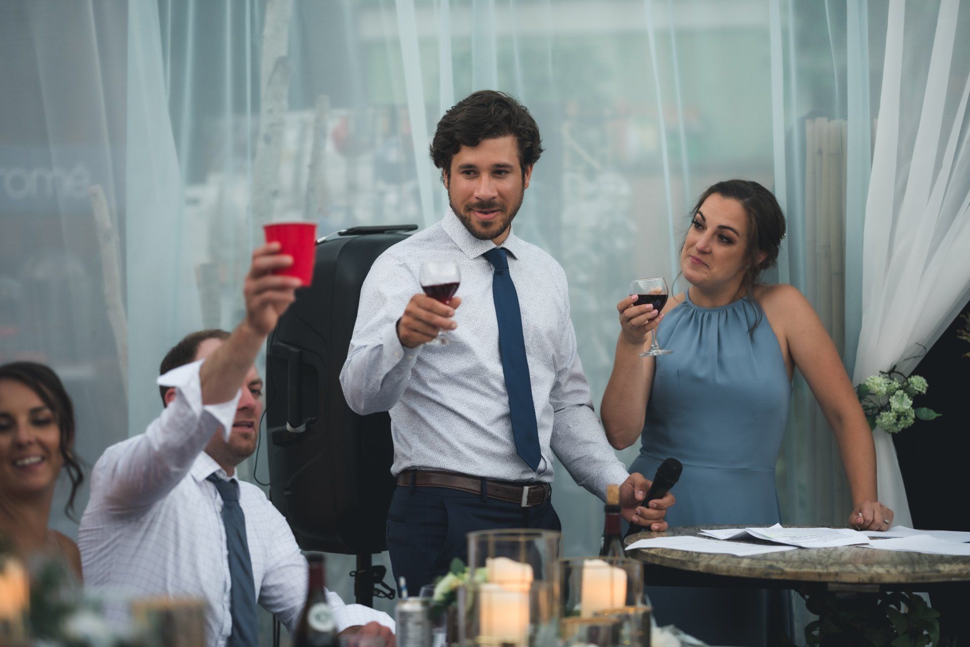 A man is giving a speech at a wedding reception while holding a glass of wine.