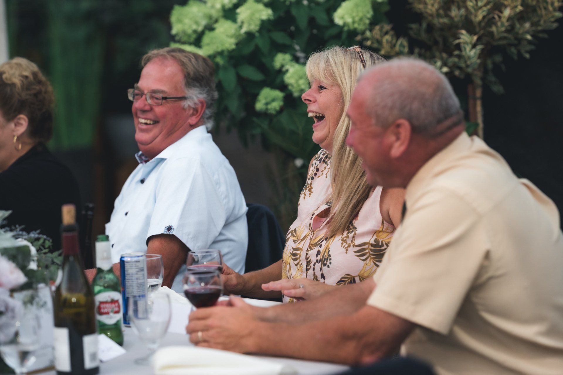 A group of people are sitting at a table laughing and drinking wine.