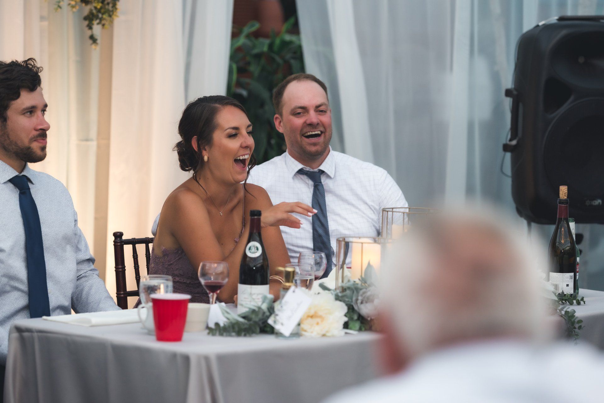 A group of people are sitting at a table laughing at a wedding reception.