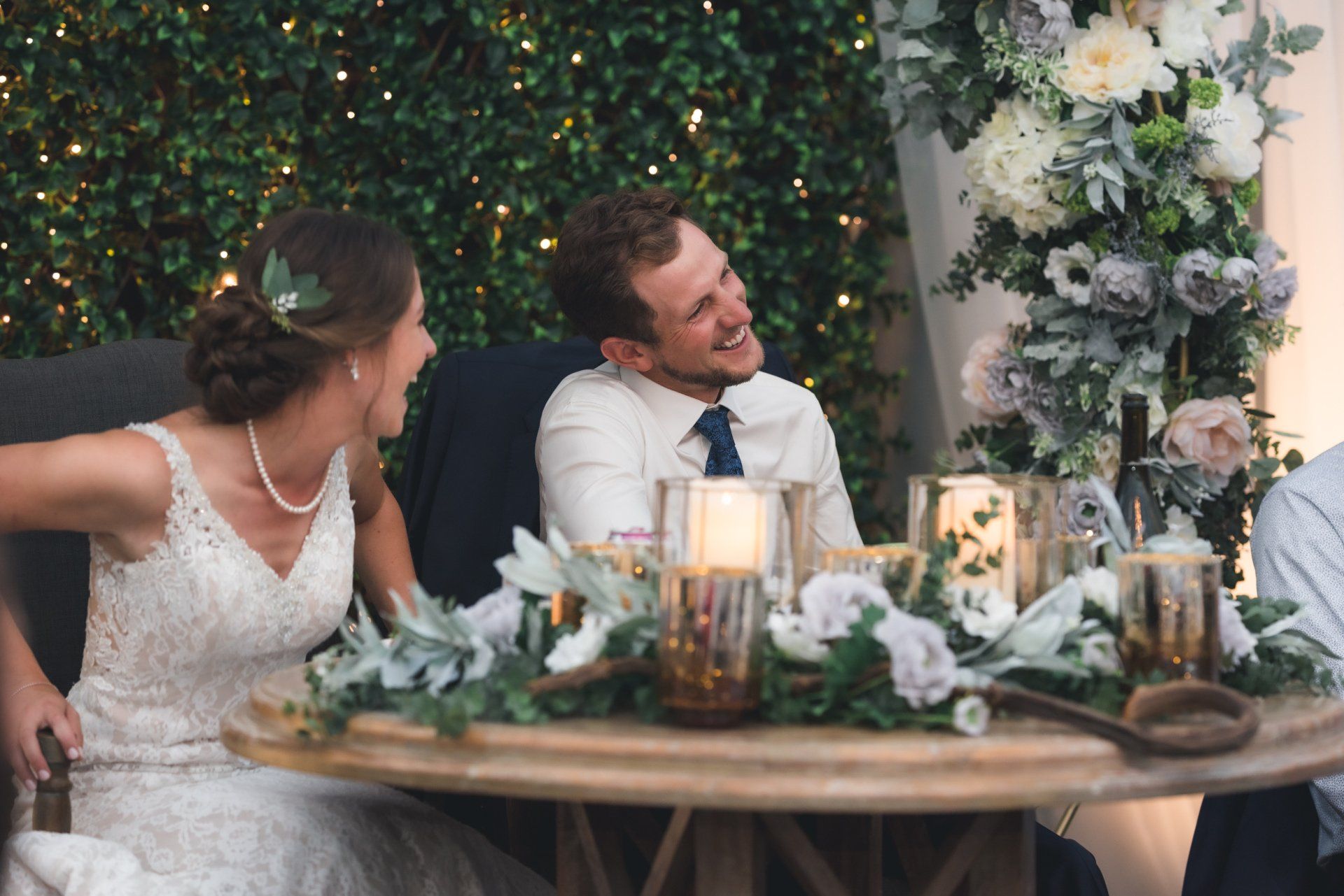 A bride and groom are sitting at a table laughing at their wedding reception.