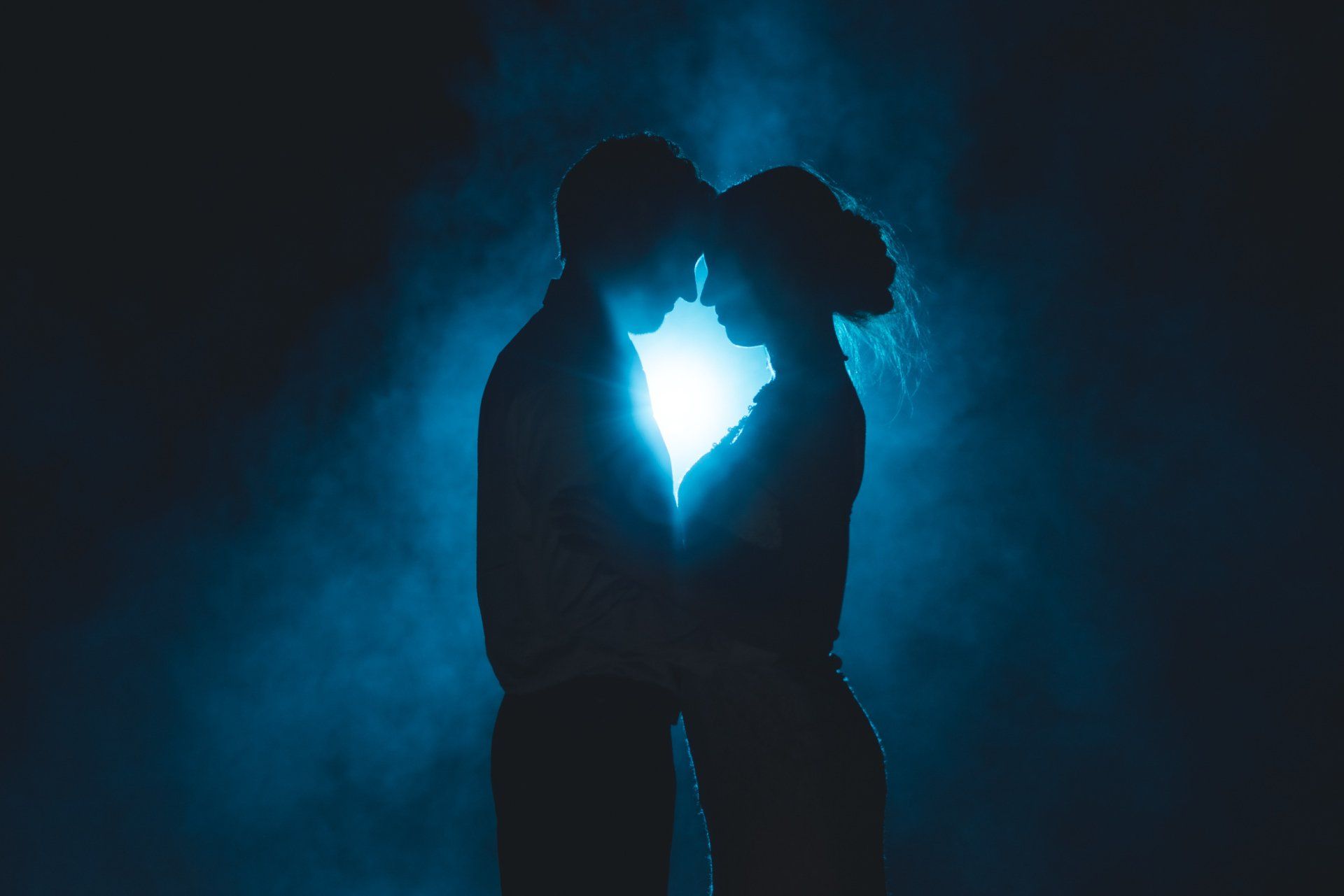 A man and a woman are kissing in the dark in front of a heart shaped light.