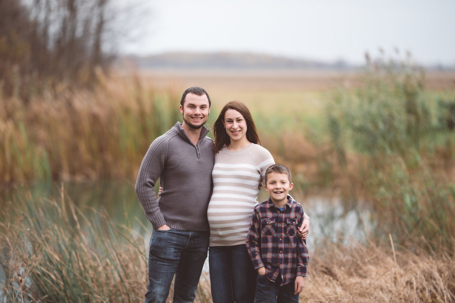 A pregnant woman , a man and a boy are posing for a picture in a field.