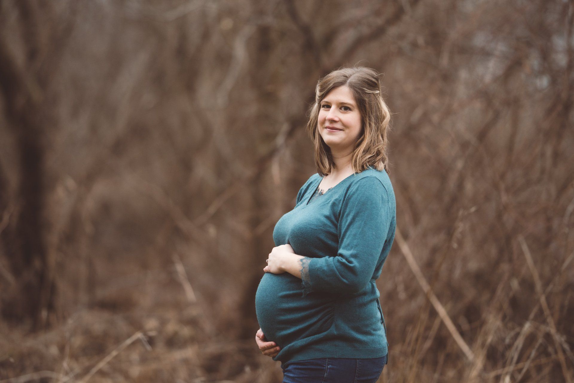 A pregnant woman is standing in a field holding her belly.
