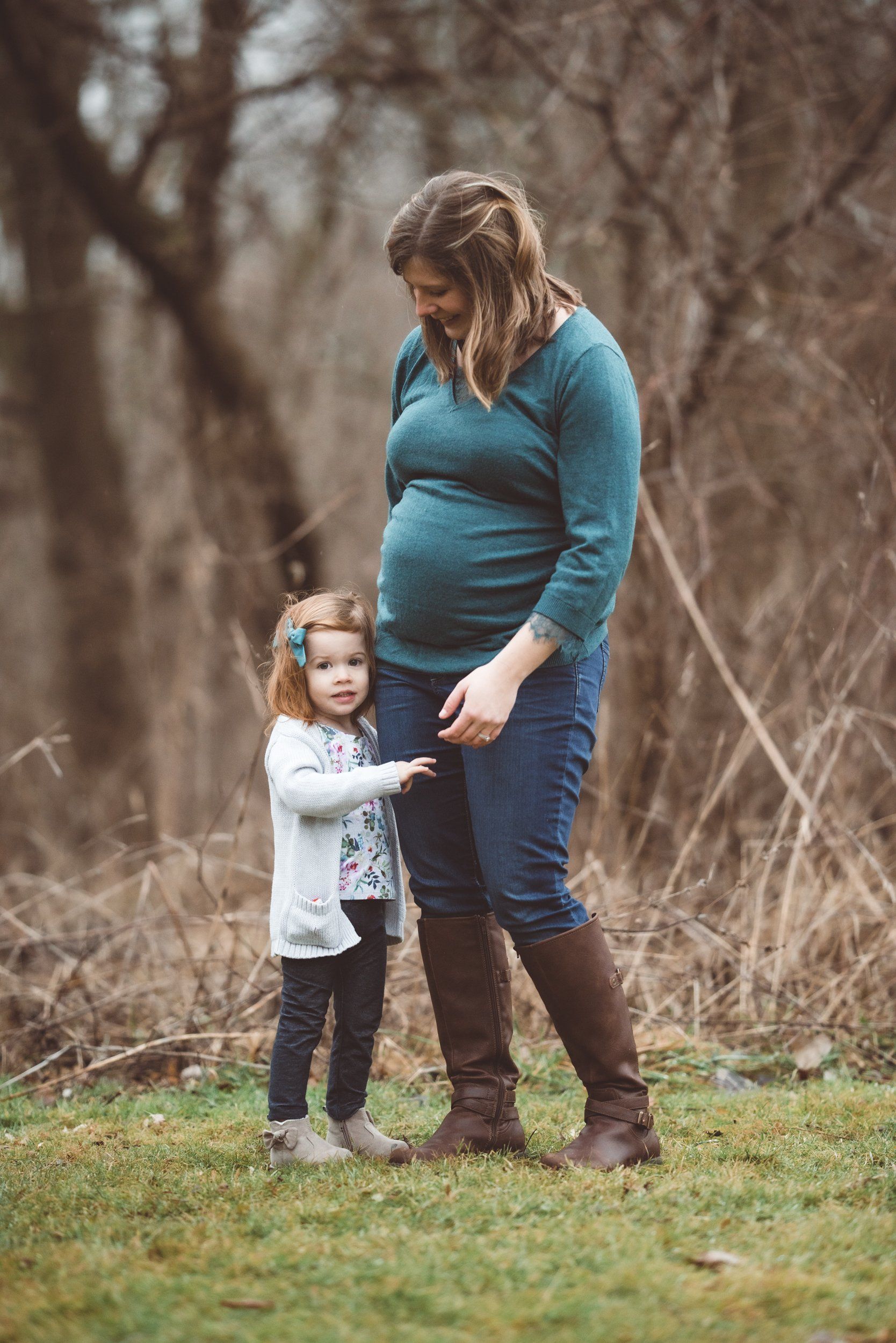 A pregnant woman is standing next to a little girl in a field.