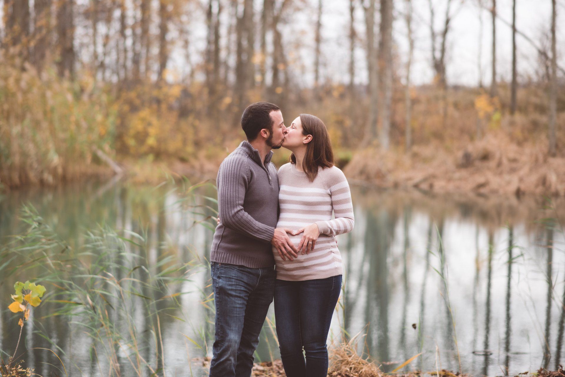A man and a pregnant woman are kissing in front of a lake.