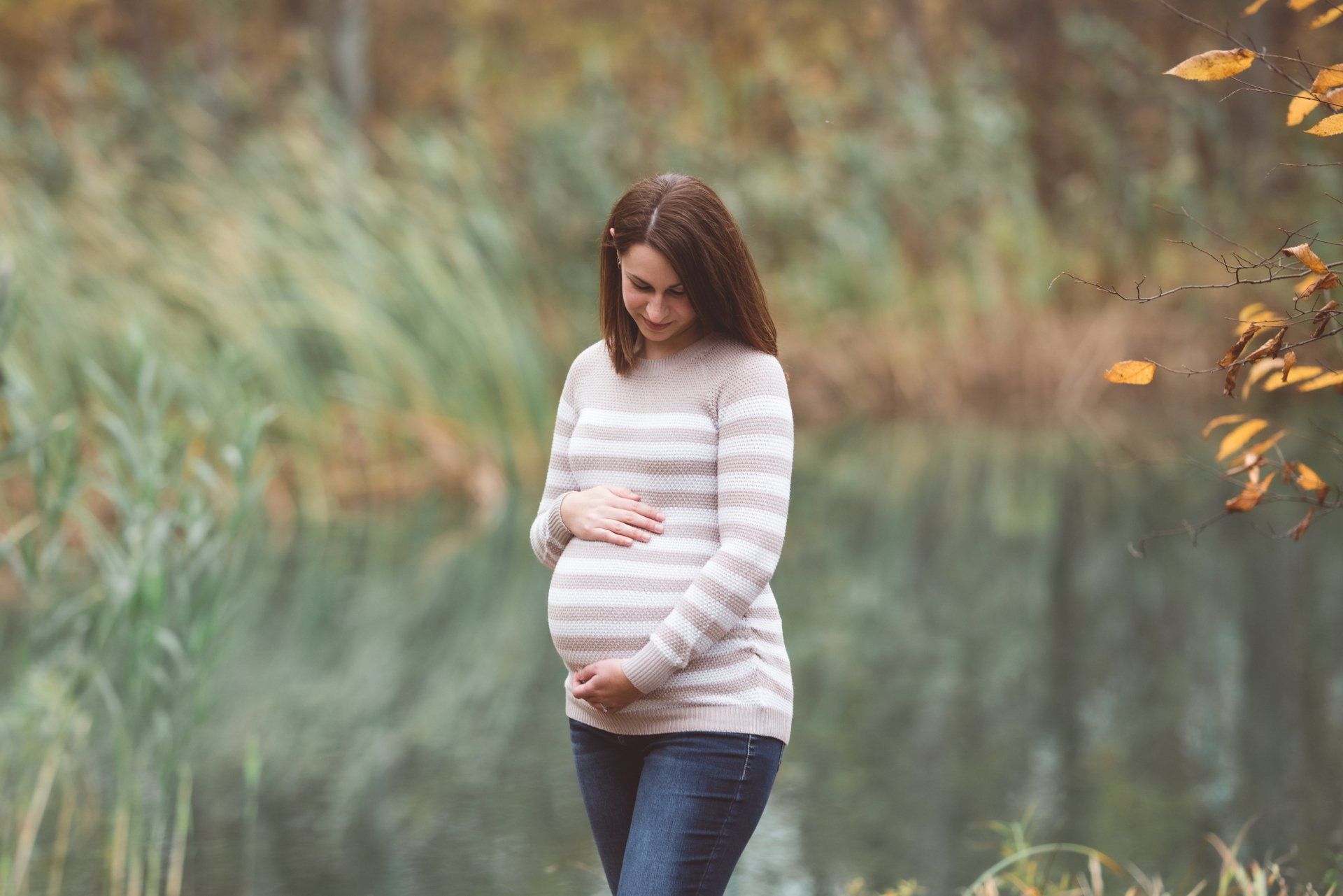 A pregnant woman is standing in a park holding her belly.