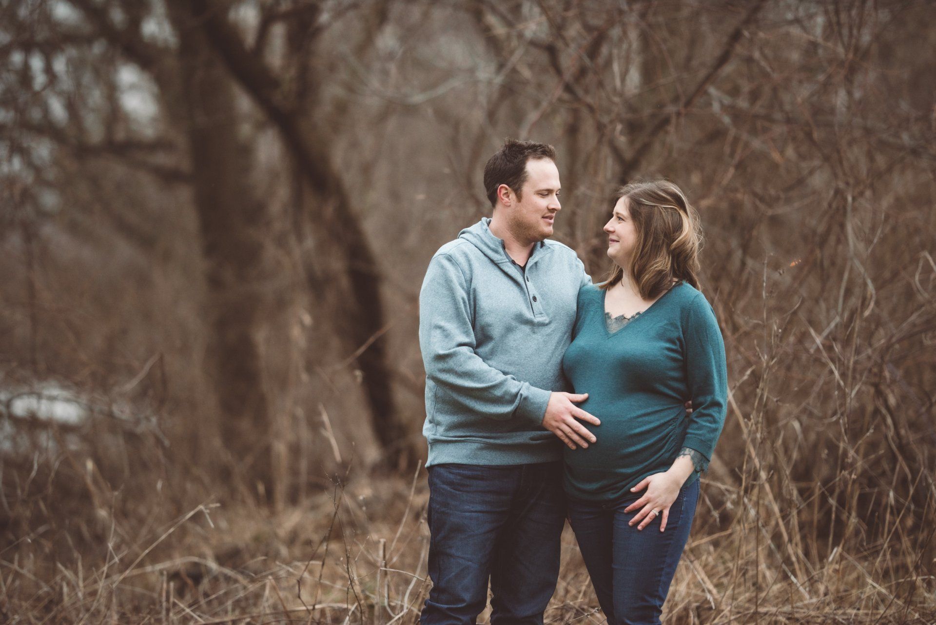 A man and a pregnant woman are standing in a field looking at each other.