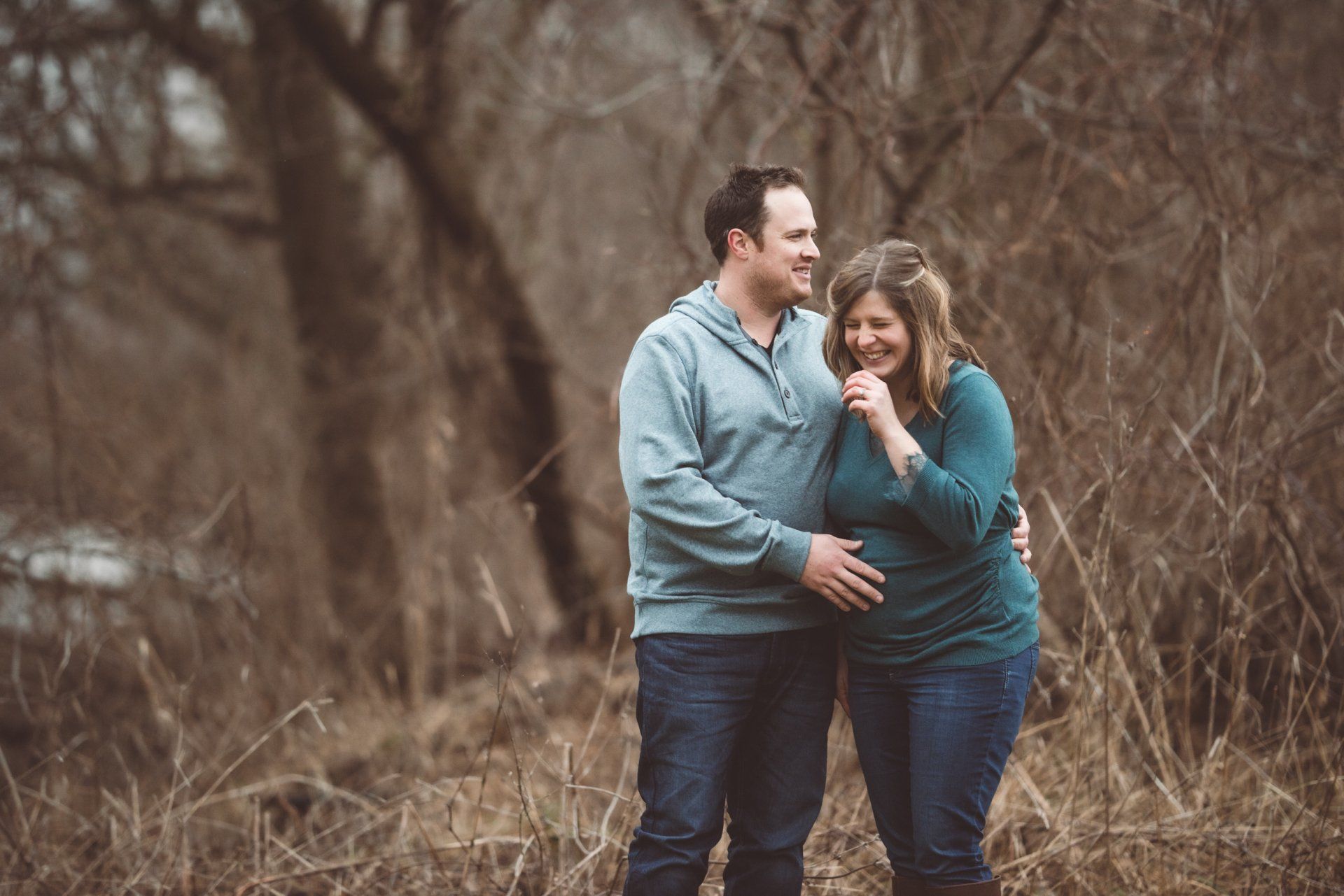 A man and a pregnant woman are standing next to each other in a field.