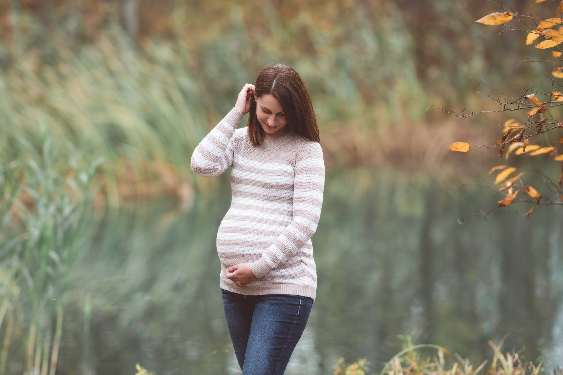A pregnant woman is walking in a park holding her belly.