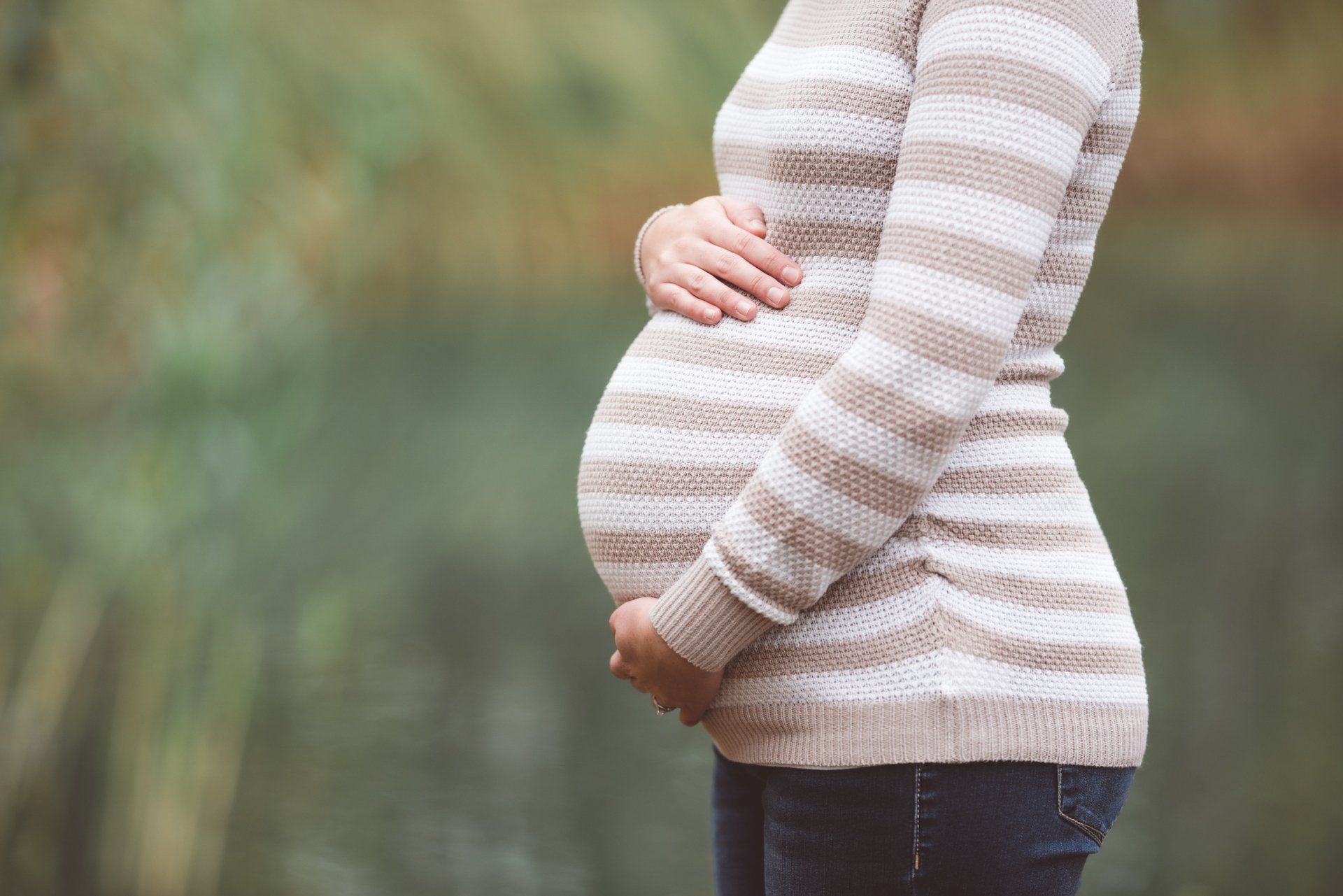 A pregnant woman in a striped sweater is holding her belly.