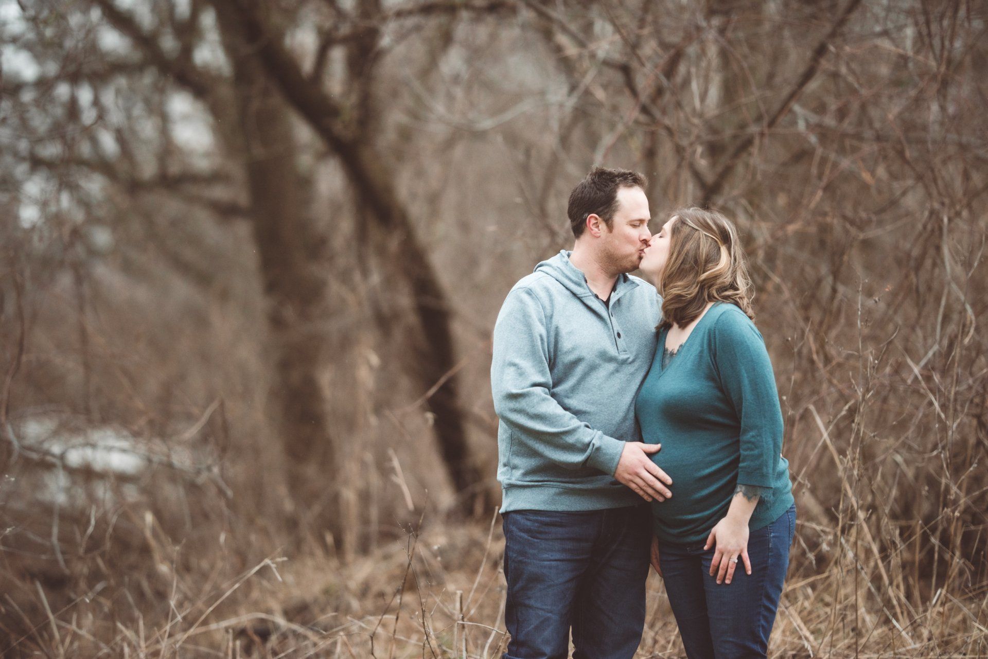 A man and a pregnant woman are kissing in a field.