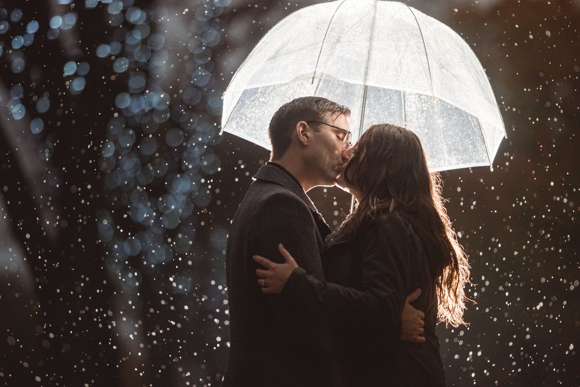 A man and a woman are kissing under an umbrella in the rain.