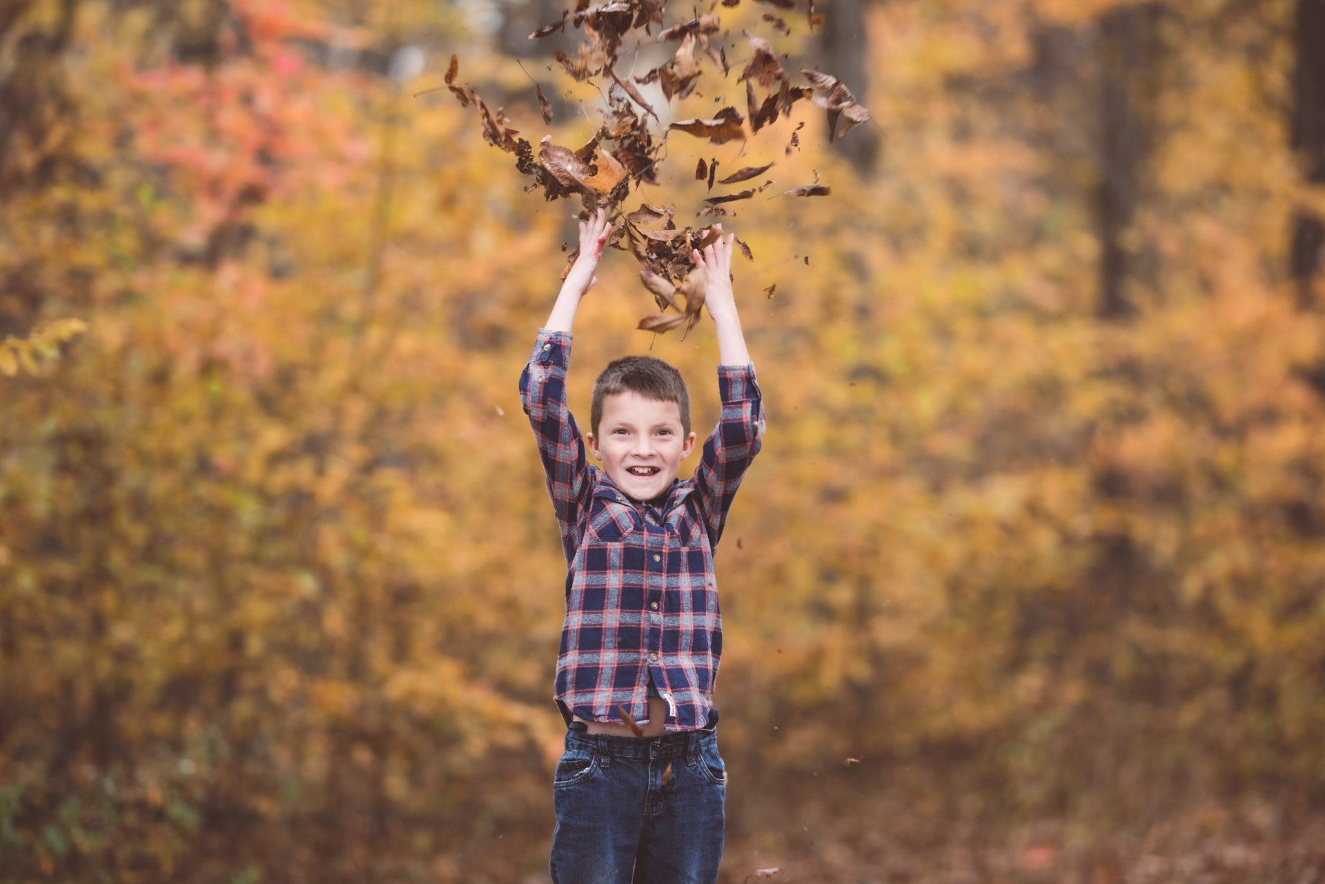 A young boy is throwing leaves in the air.