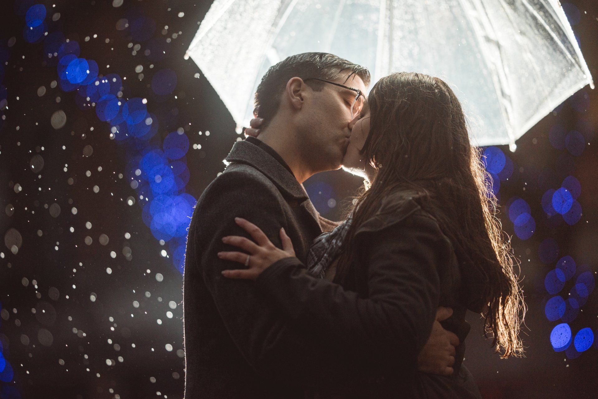 A man and a woman are kissing under an umbrella in the rain.