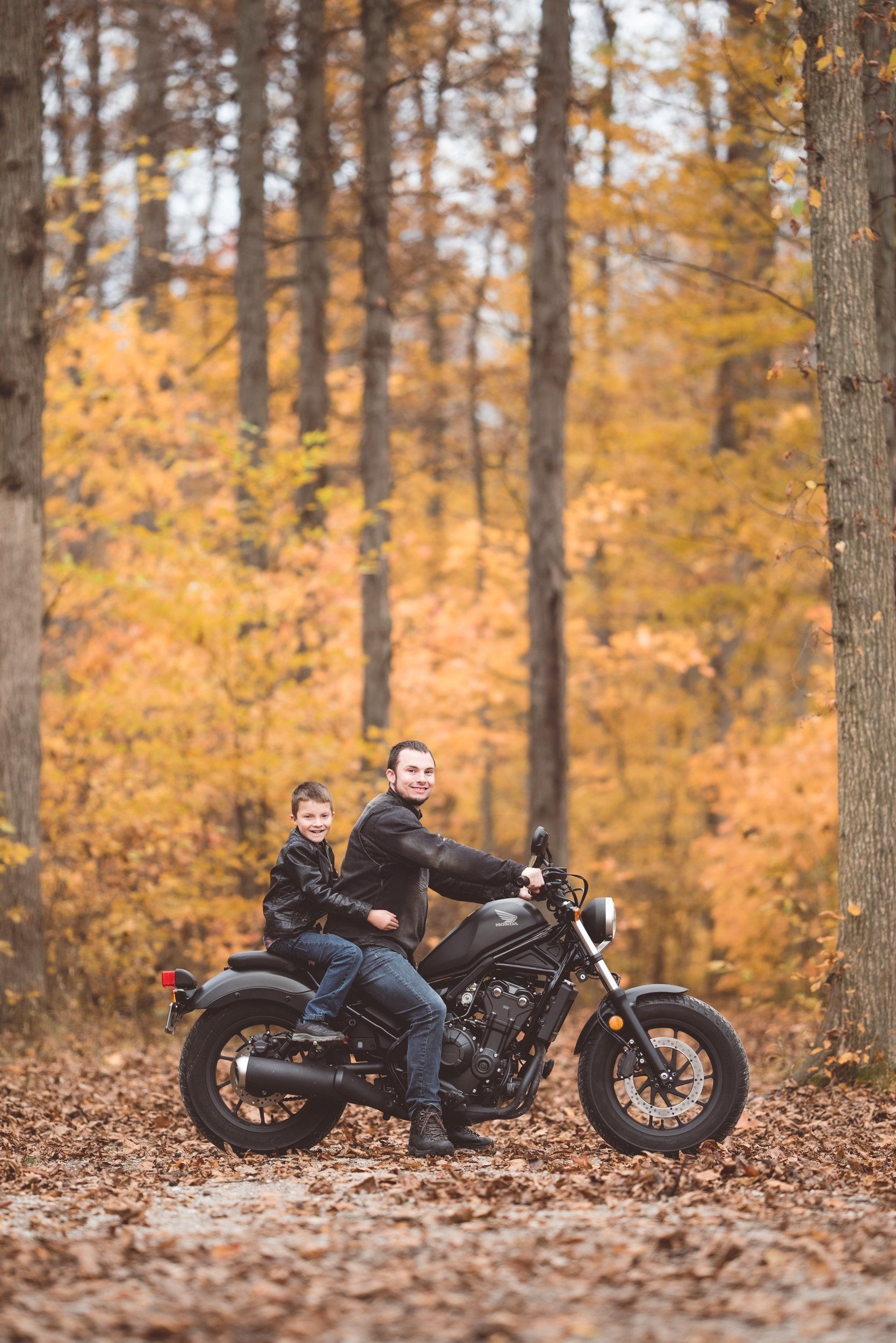 A man and a boy are riding a motorcycle in the woods.