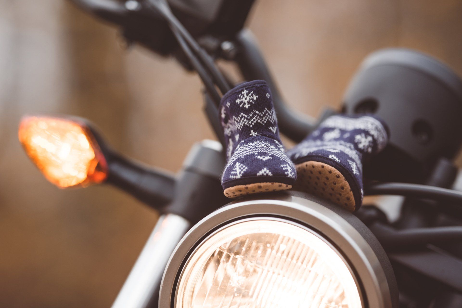 A baby 's feet are sitting on the headlight of a motorcycle.