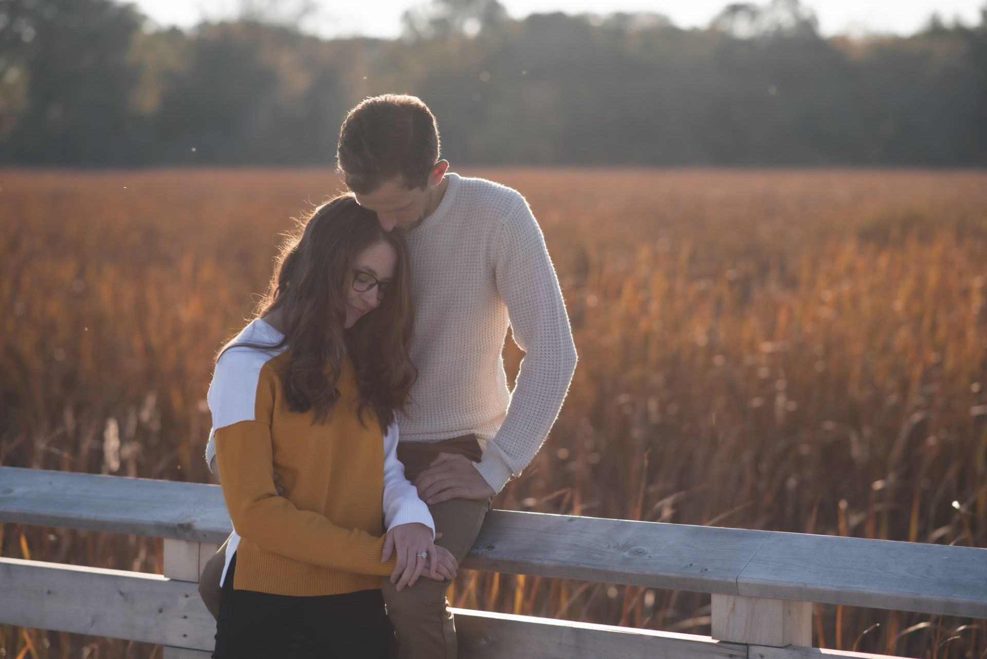 A man and a woman are standing next to each other on a fence in a field.