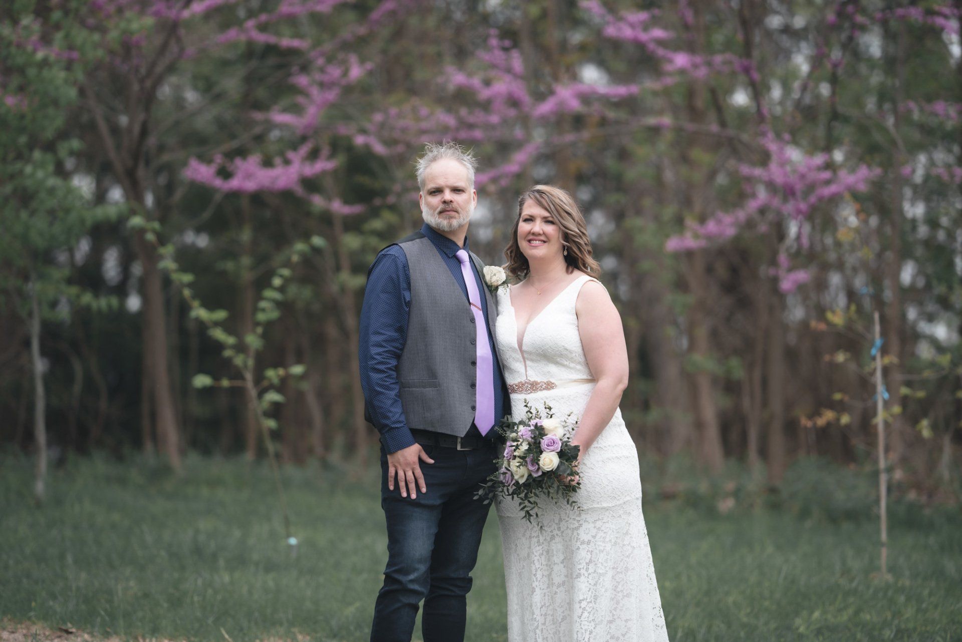 A bride and groom are posing for a picture in front of purple flowers.