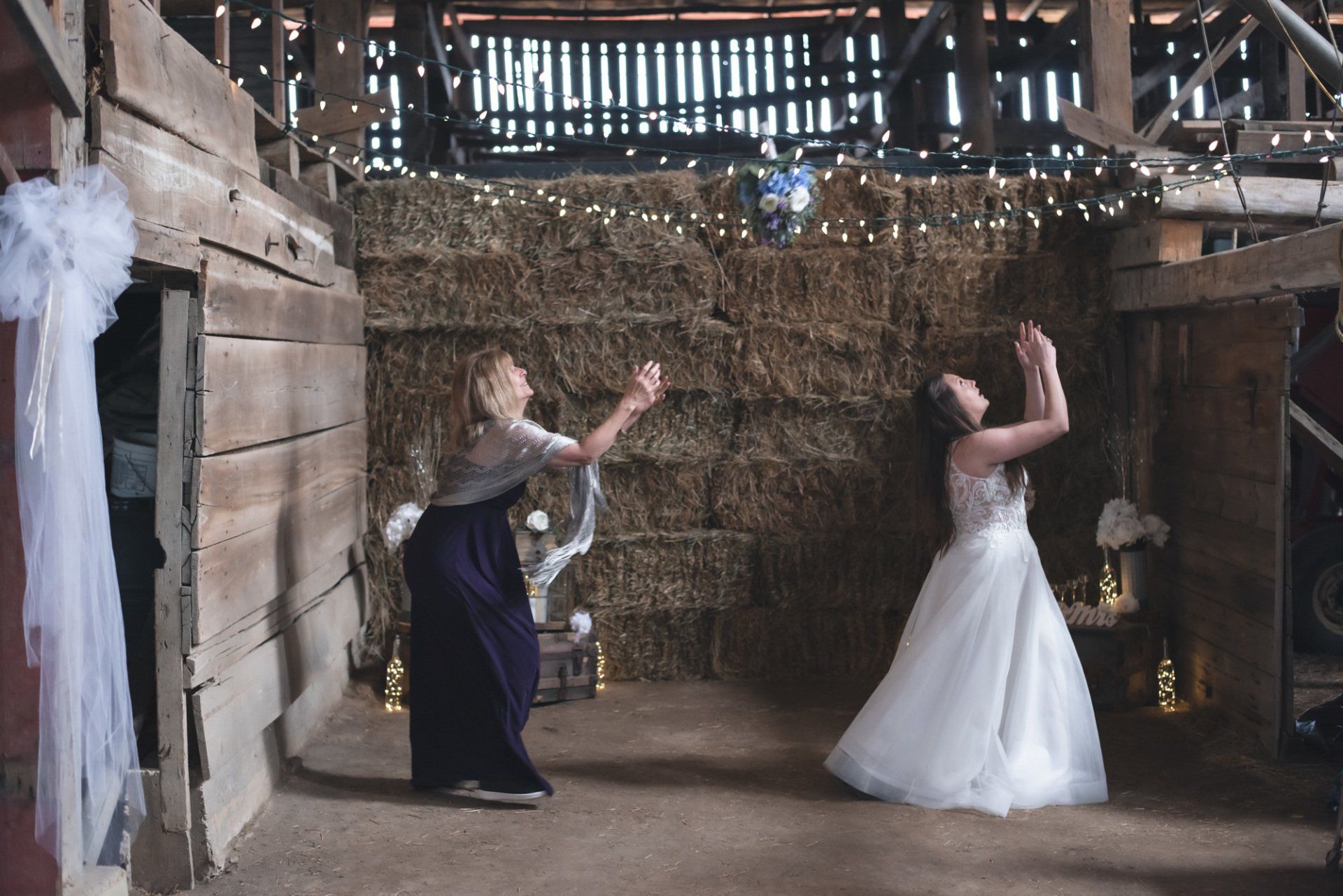 A bride and her mother are dancing in a barn.