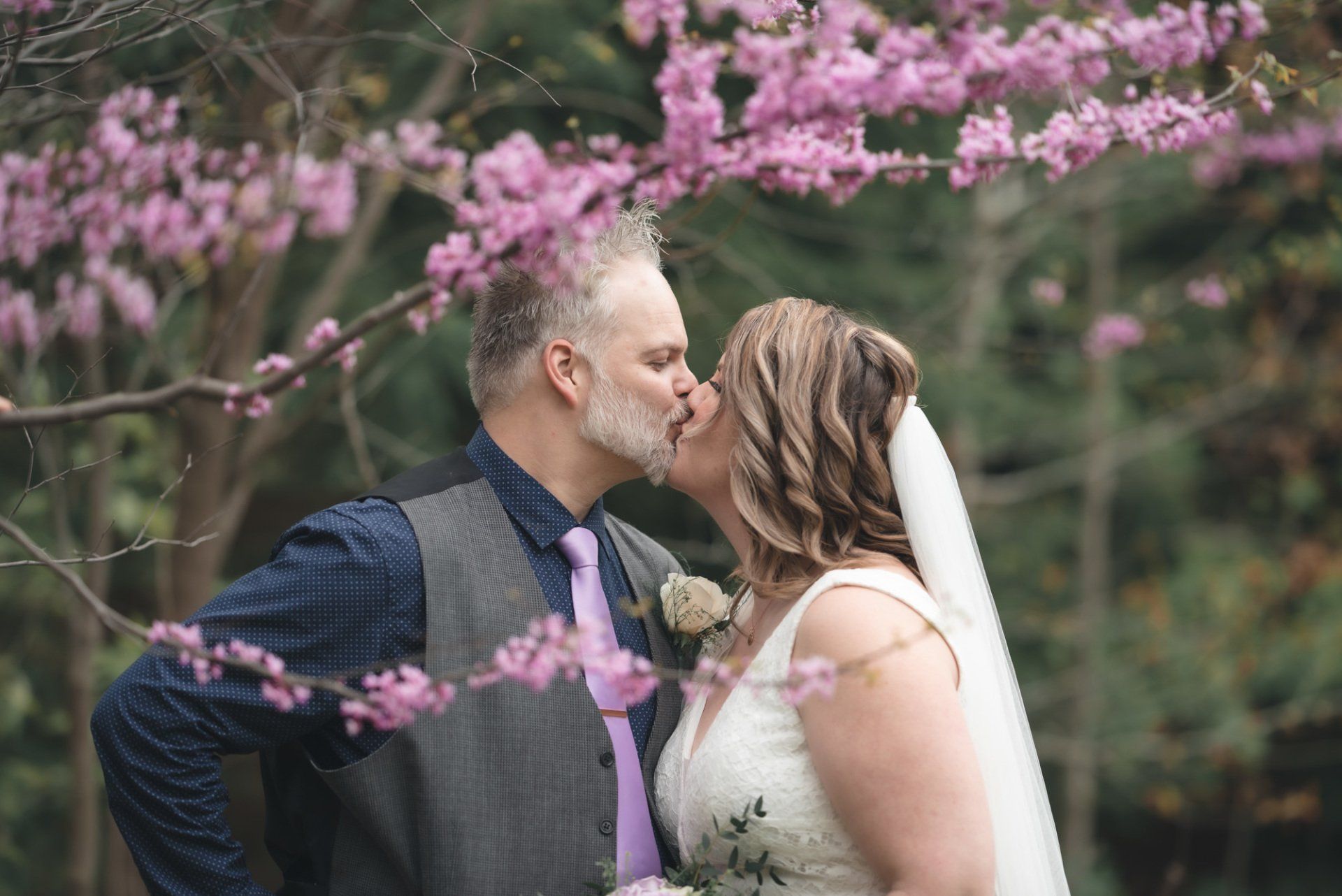 A bride and groom are kissing under a tree with pink flowers.