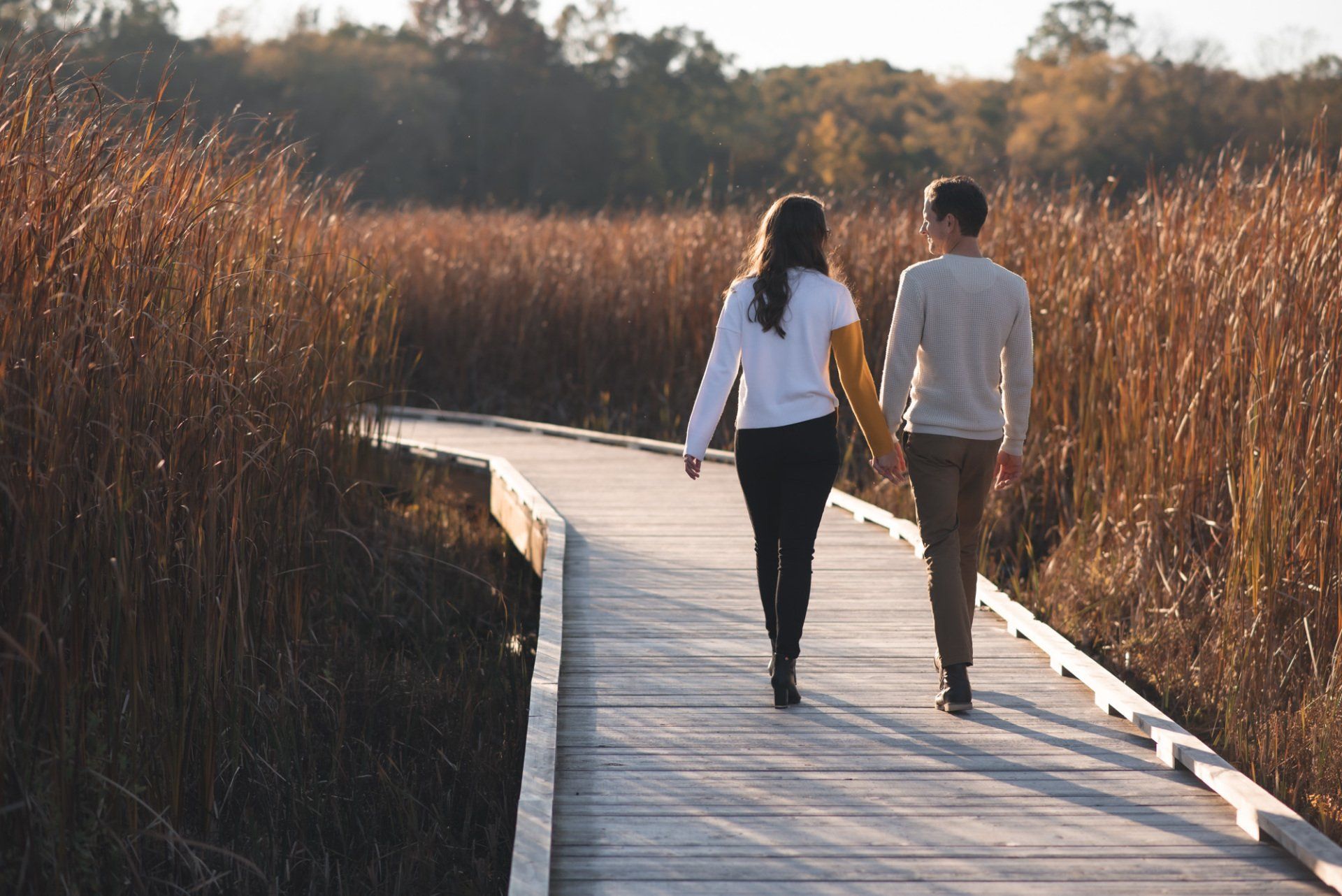 Two women are walking down a wooden boardwalk holding hands
